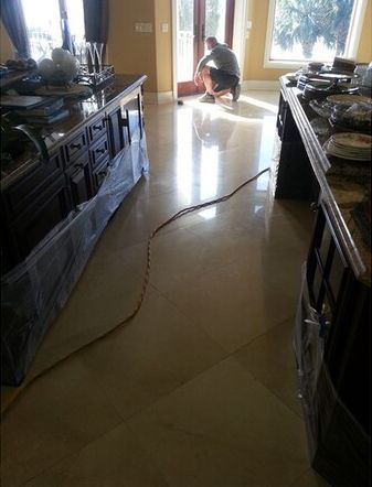 A man is kneeling on a tiled floor in a kitchen.
