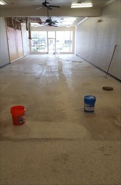 A large empty room with two buckets and a mop on the floor.