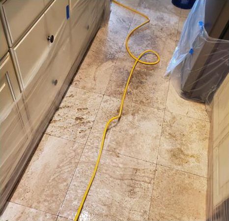 A yellow power cord is laying on a tiled floor in a kitchen.