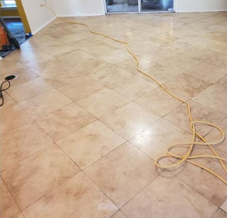 A vacuum cleaner is sitting on a tiled floor next to a power cord.