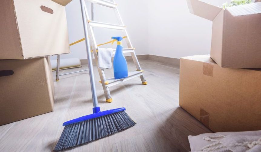 A broom is sitting on the floor next to a ladder and boxes.