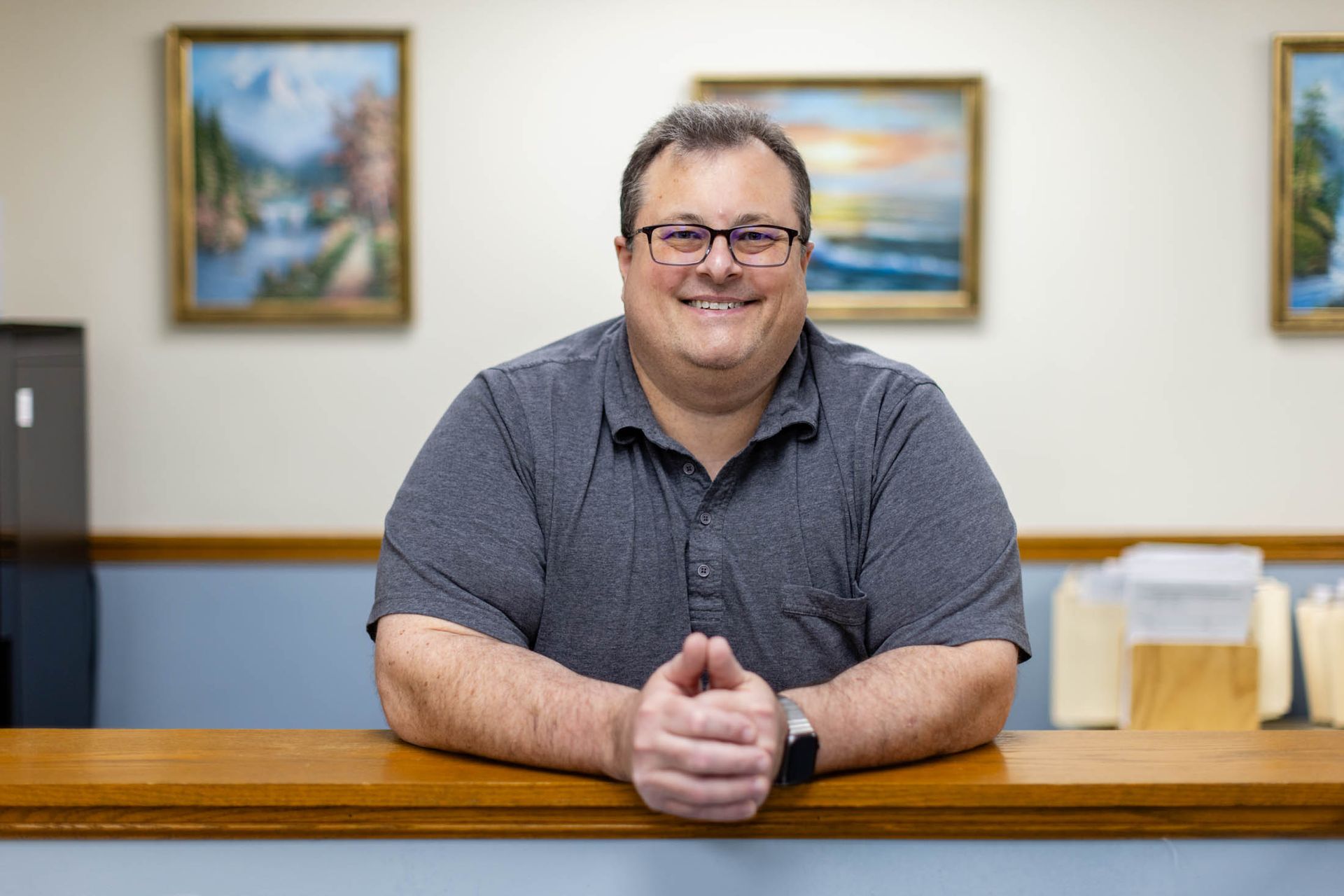 Blond woman smiling, wearing a black top, against a dark gray backdrop.
