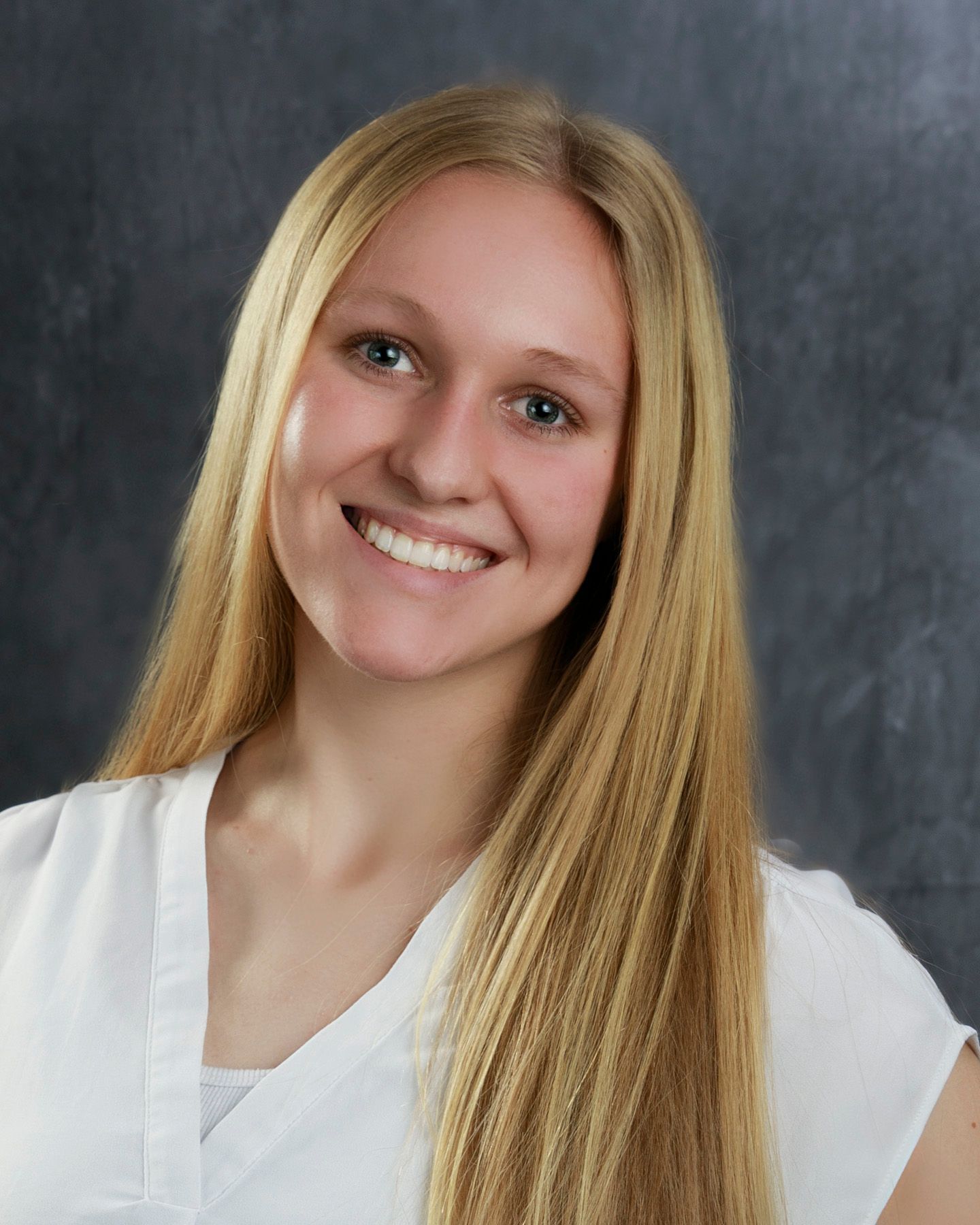 Blonde woman smiling, wearing a white top, against a gray background.