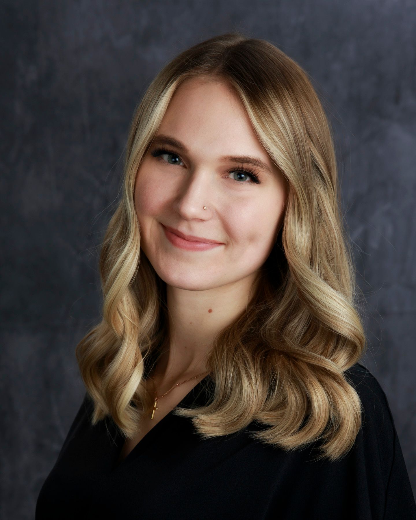 Blond woman smiling, wearing a black top, against a dark gray backdrop.