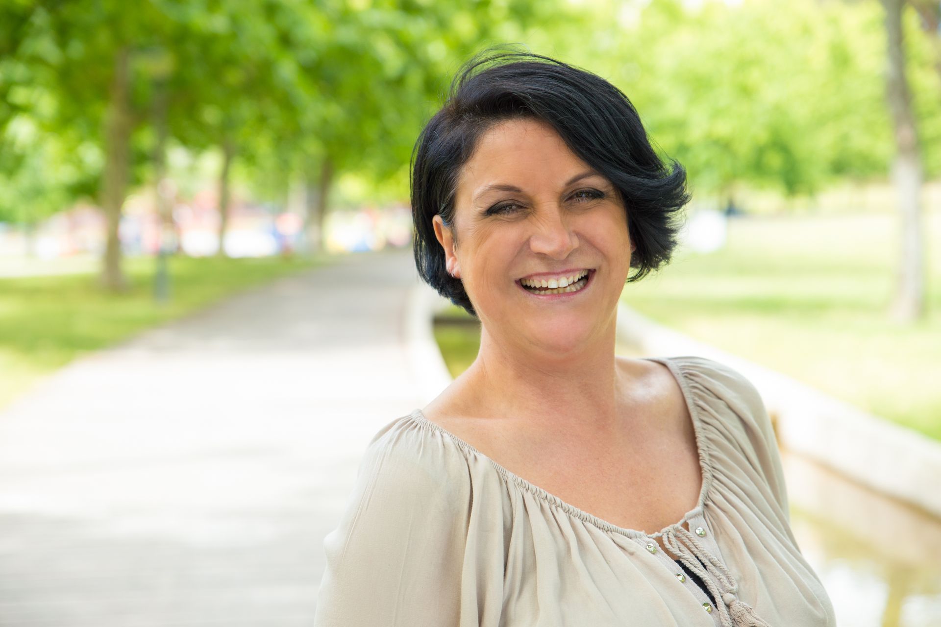 a woman with short black hair is smiling in a park