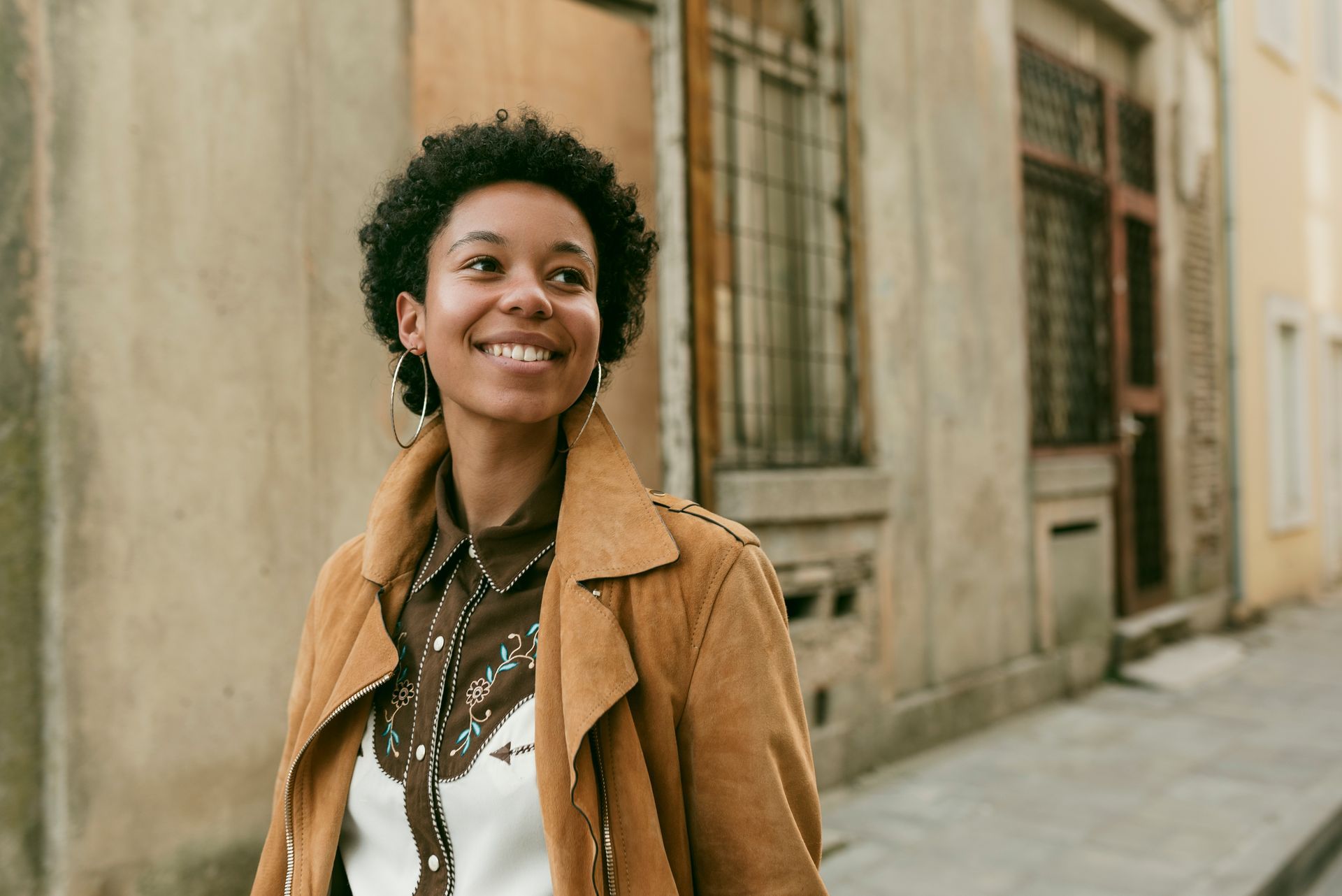 a woman in a brown jacket is smiling in front of a building
