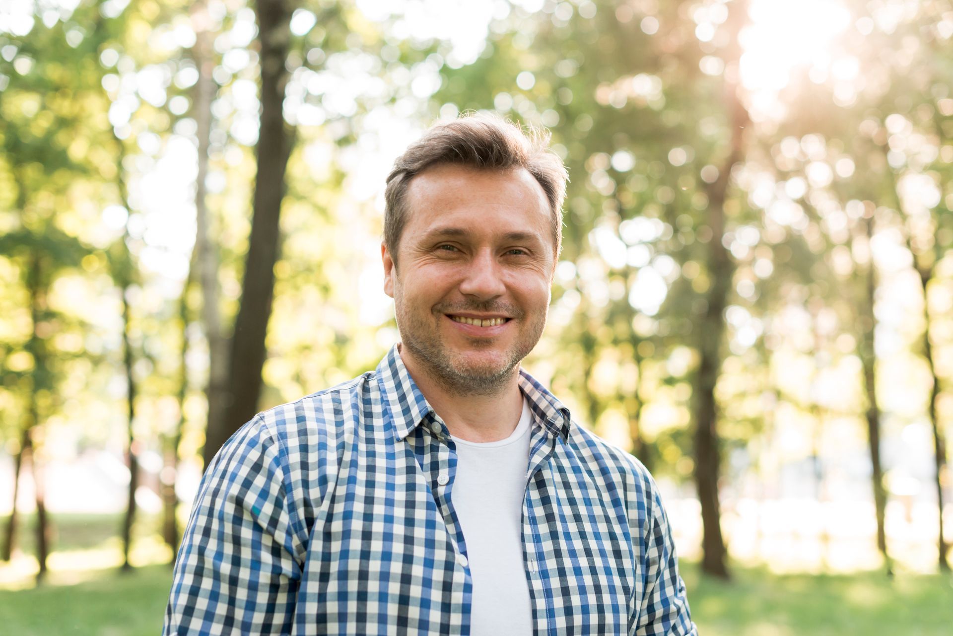 a man in a plaid shirt is smiling in front of trees