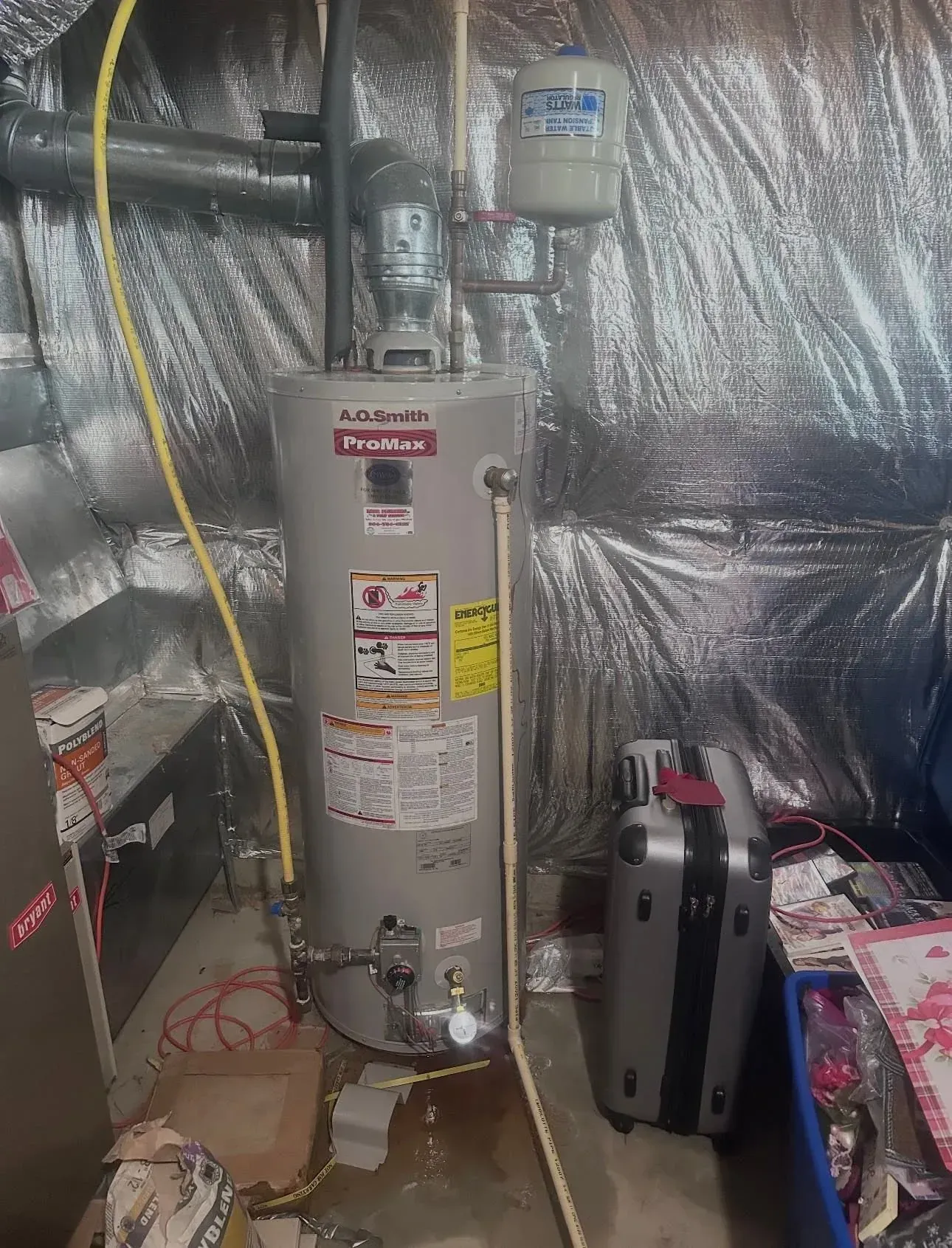 Water heater in a basement utility area with foil insulation and a tool case on the floor. Water heater in a basement utility area with foil insulation and a tool case on the floor.