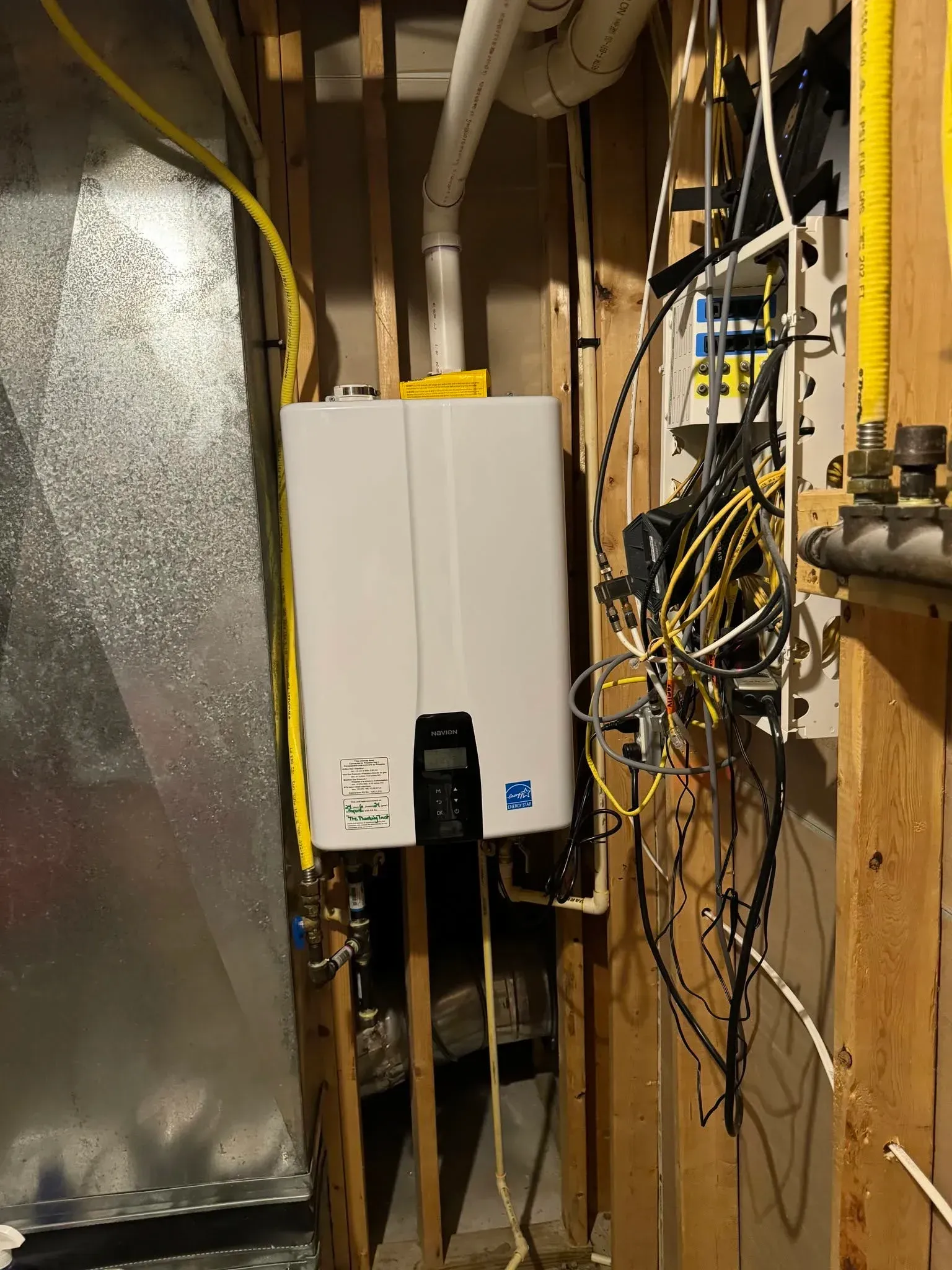 Basement utility wall with white electrical panel, exposed wiring, and metal ducting. Basement utility wall with white electrical panel, exposed wiring, and metal ducting.