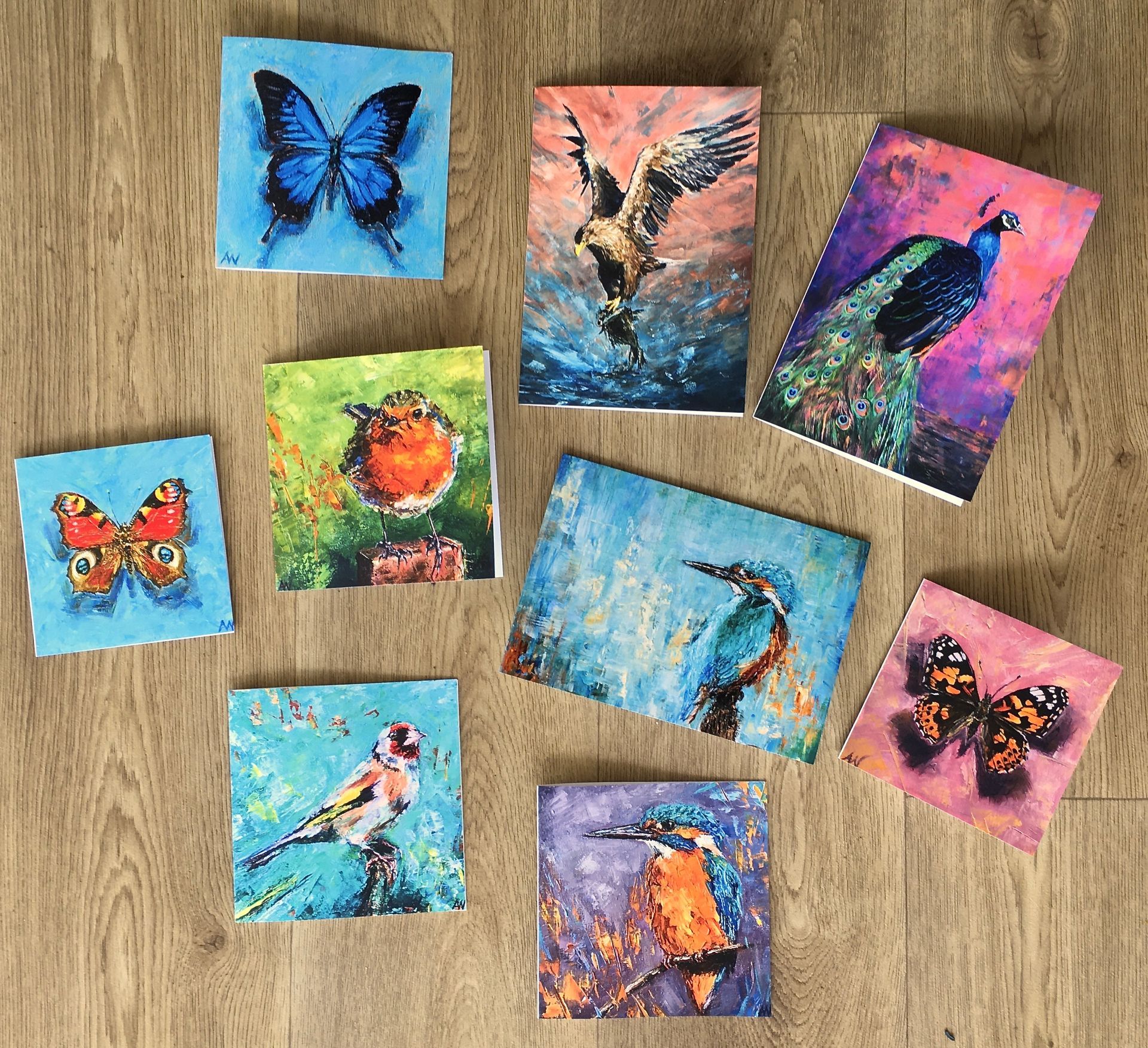 Schilderijen van vogels en vlinders op vierkante doeken, gerangschikt op een houten vloer.
