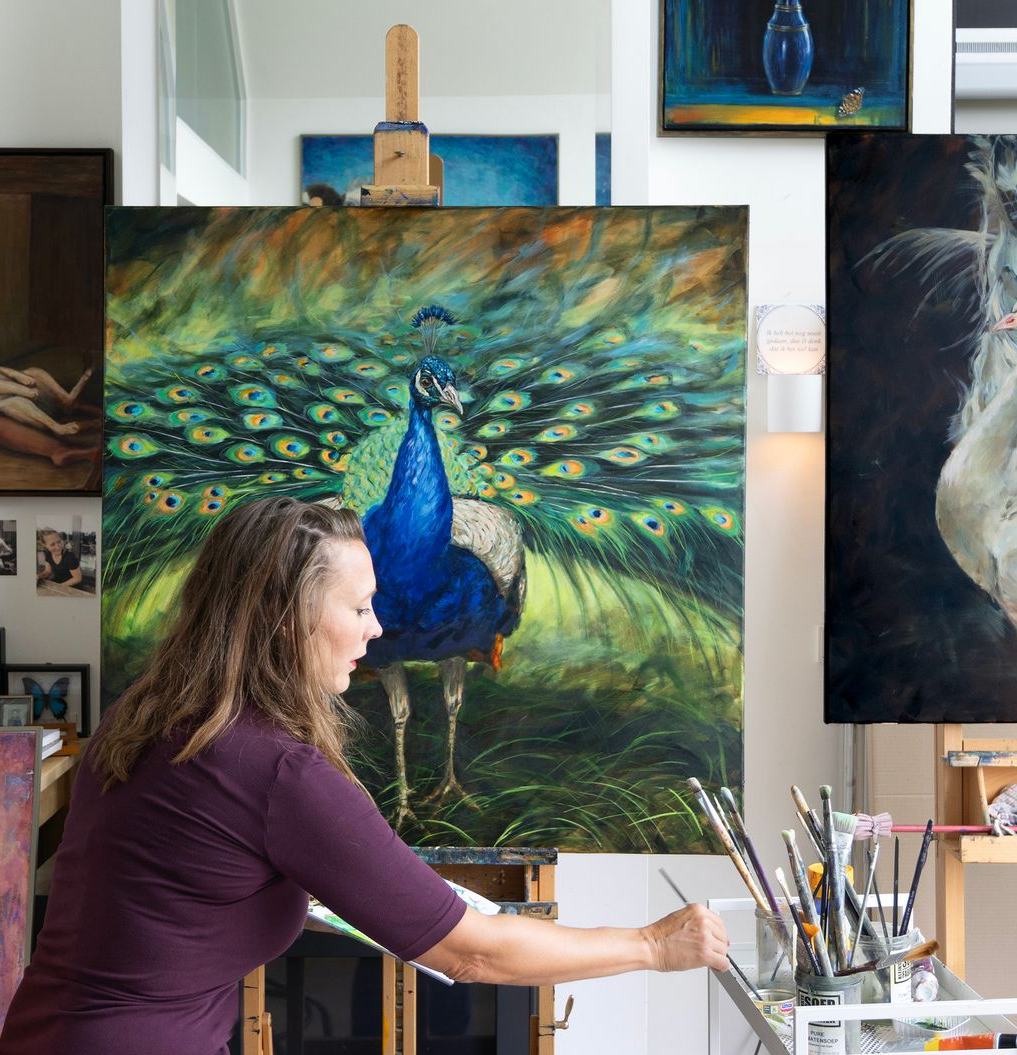 Woman painting a peacock with brushes; studio setting with other art.
