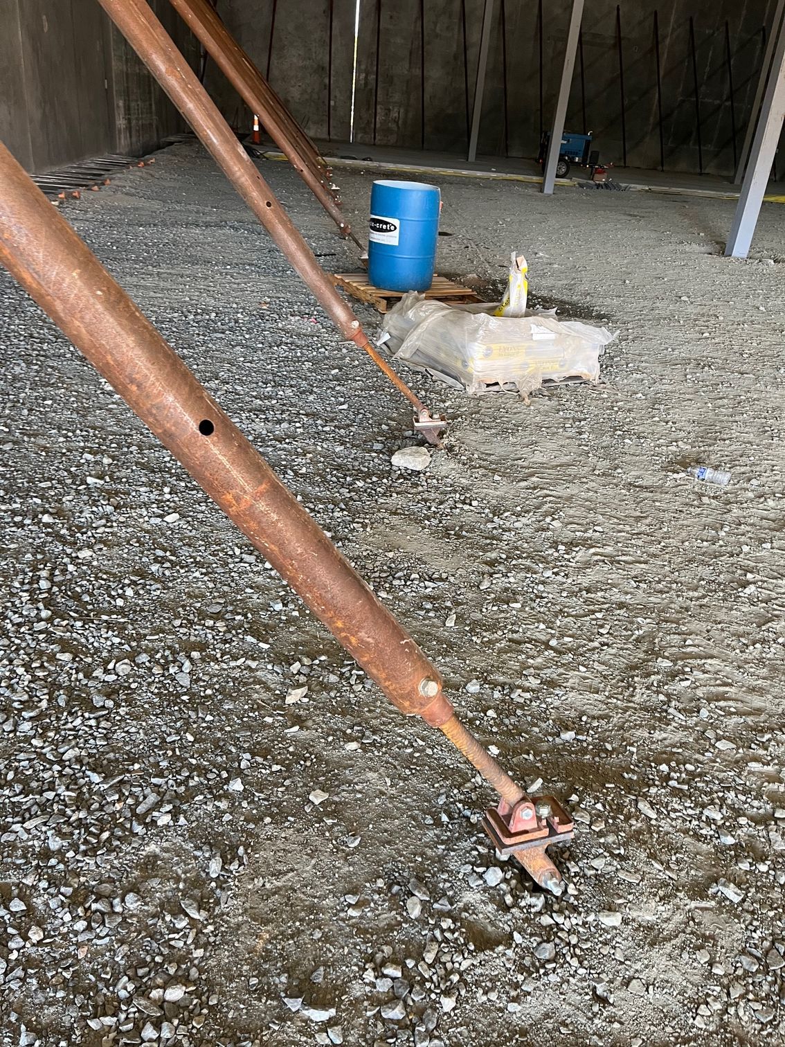 Brown metal poles set on gravel floor with blue barrel in background.