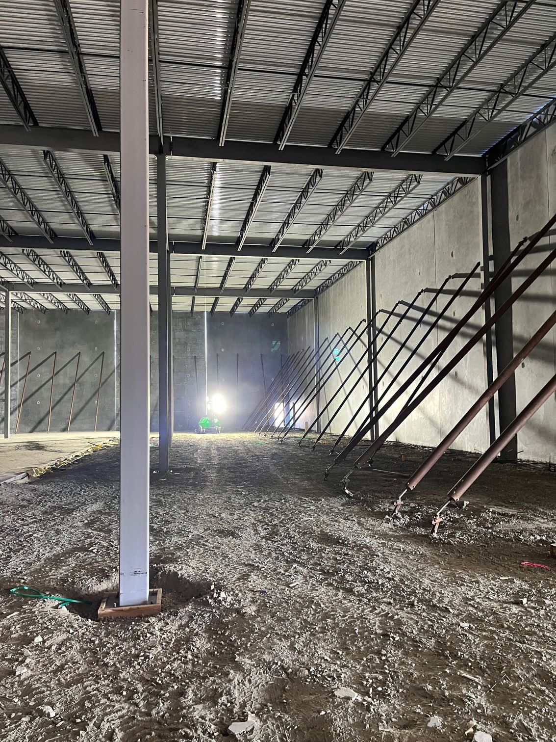 Interior of a warehouse under construction, with steel beams, concrete walls, and gravel floor.