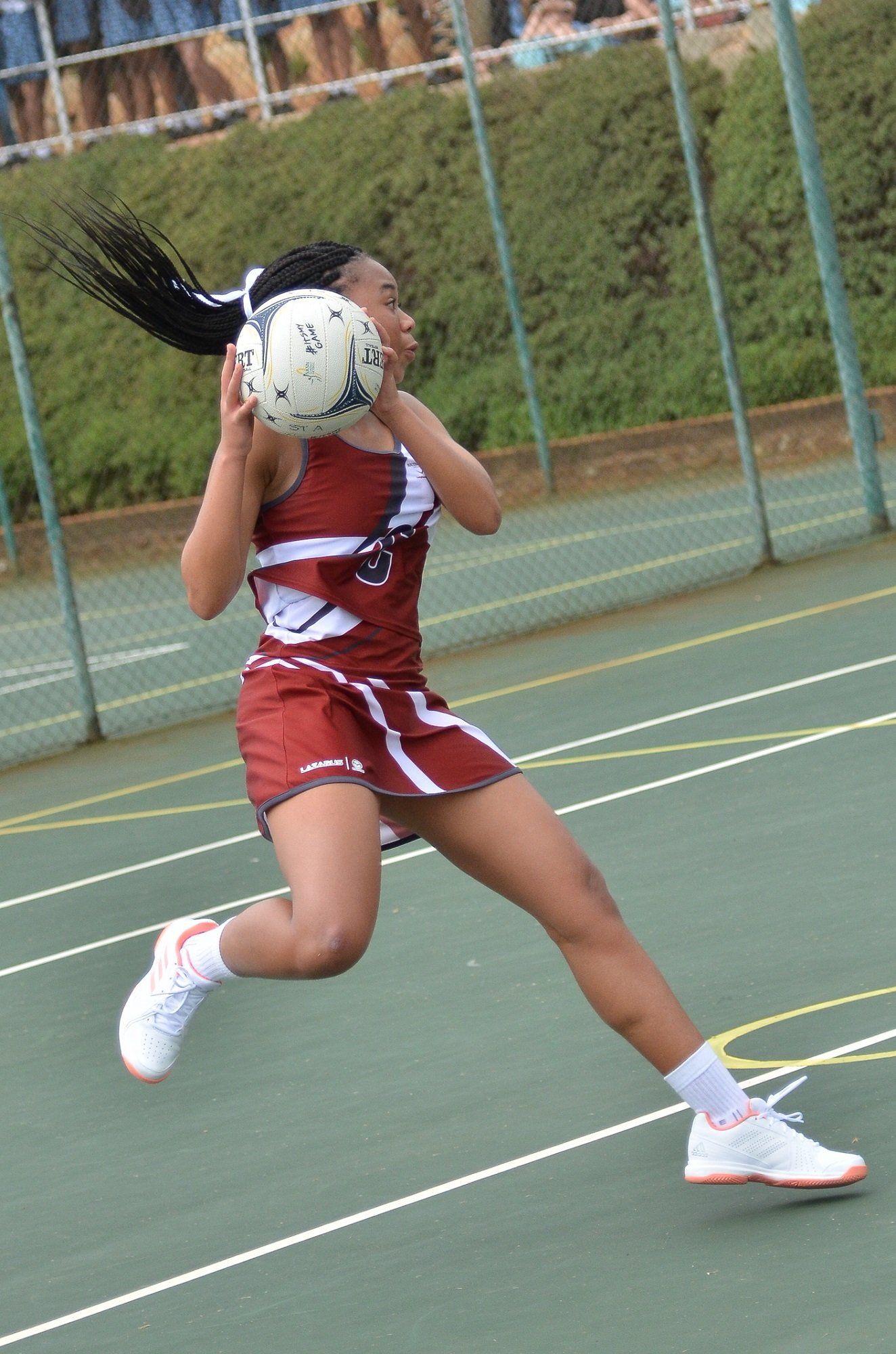 A girl in a red and white uniform is holding a netball in her hands.
