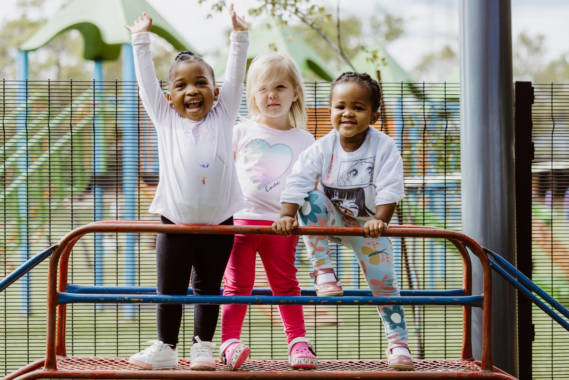 Three little girls are standing on a monkey bars at a playground.