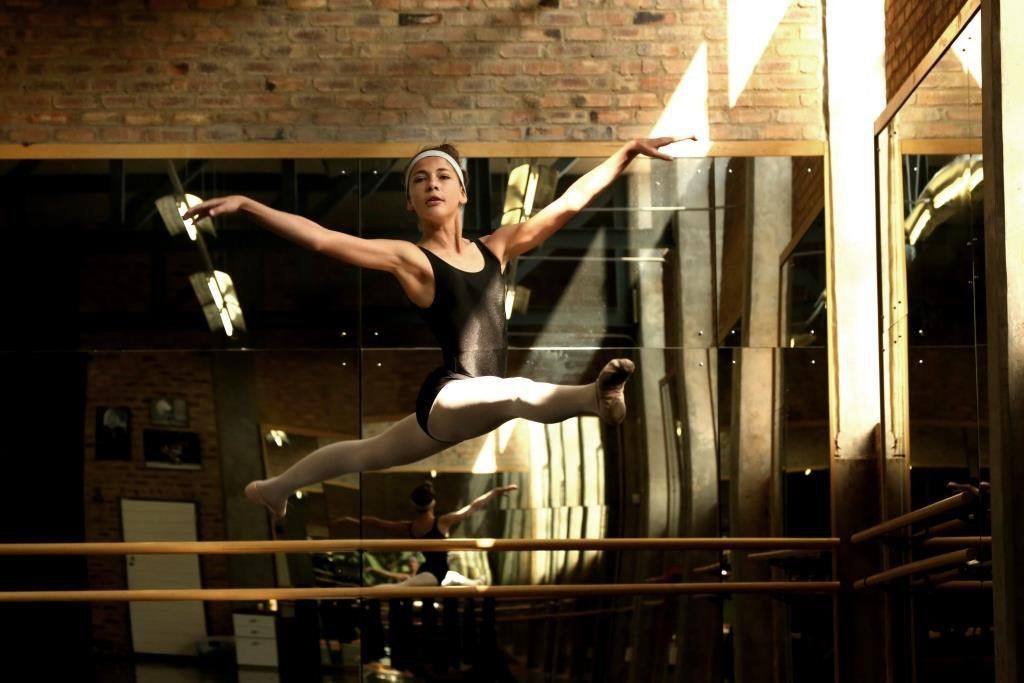 A ballerina is jumping in the air in front of a mirror in a dance studio.