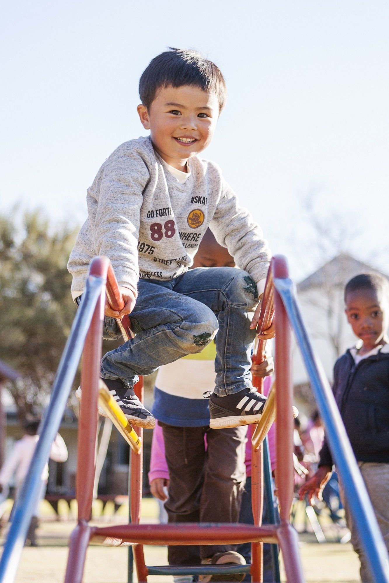 A young boy is sitting on top of a slide at a playground.
