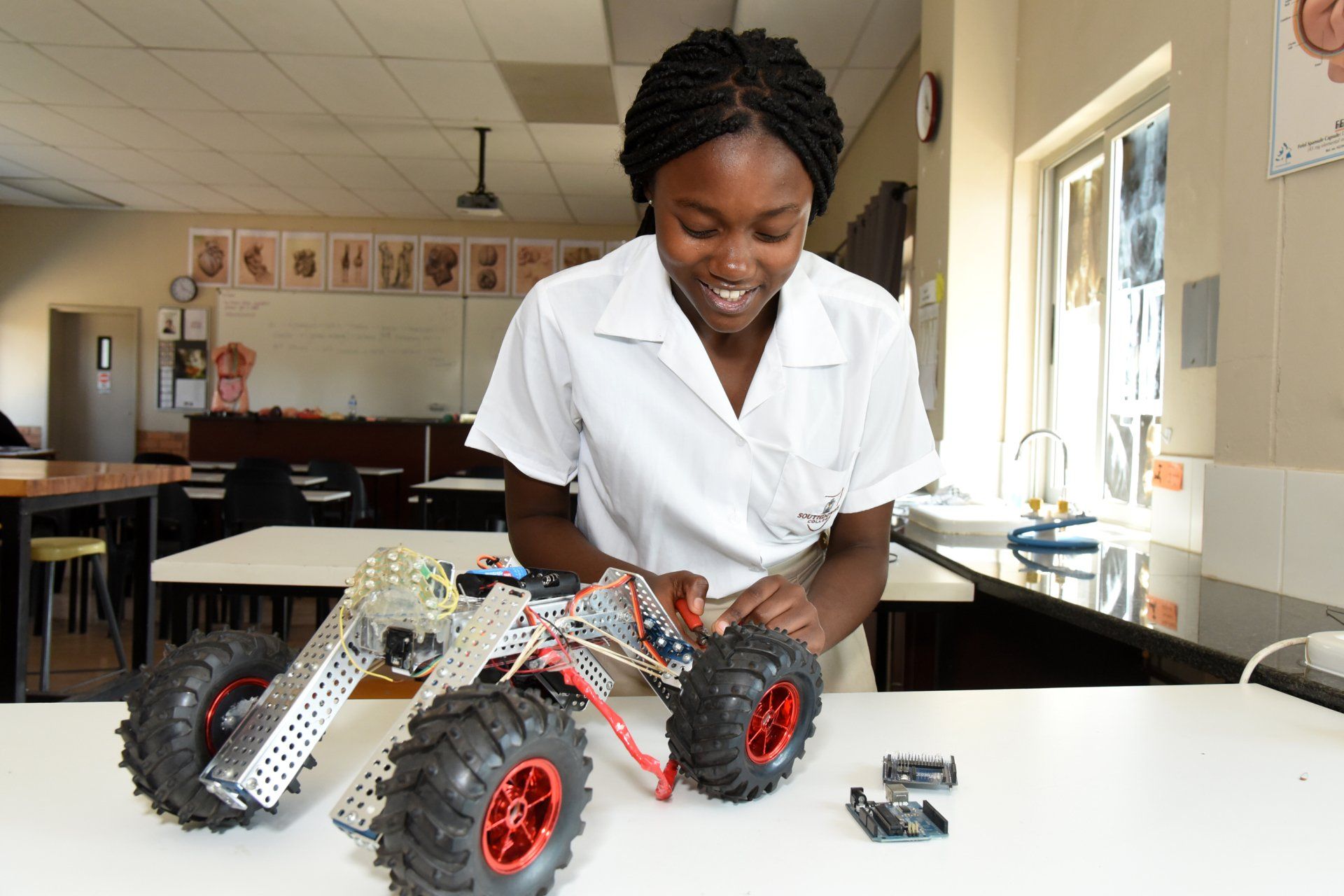 A woman is working on a robotic vehicle in a classroom.