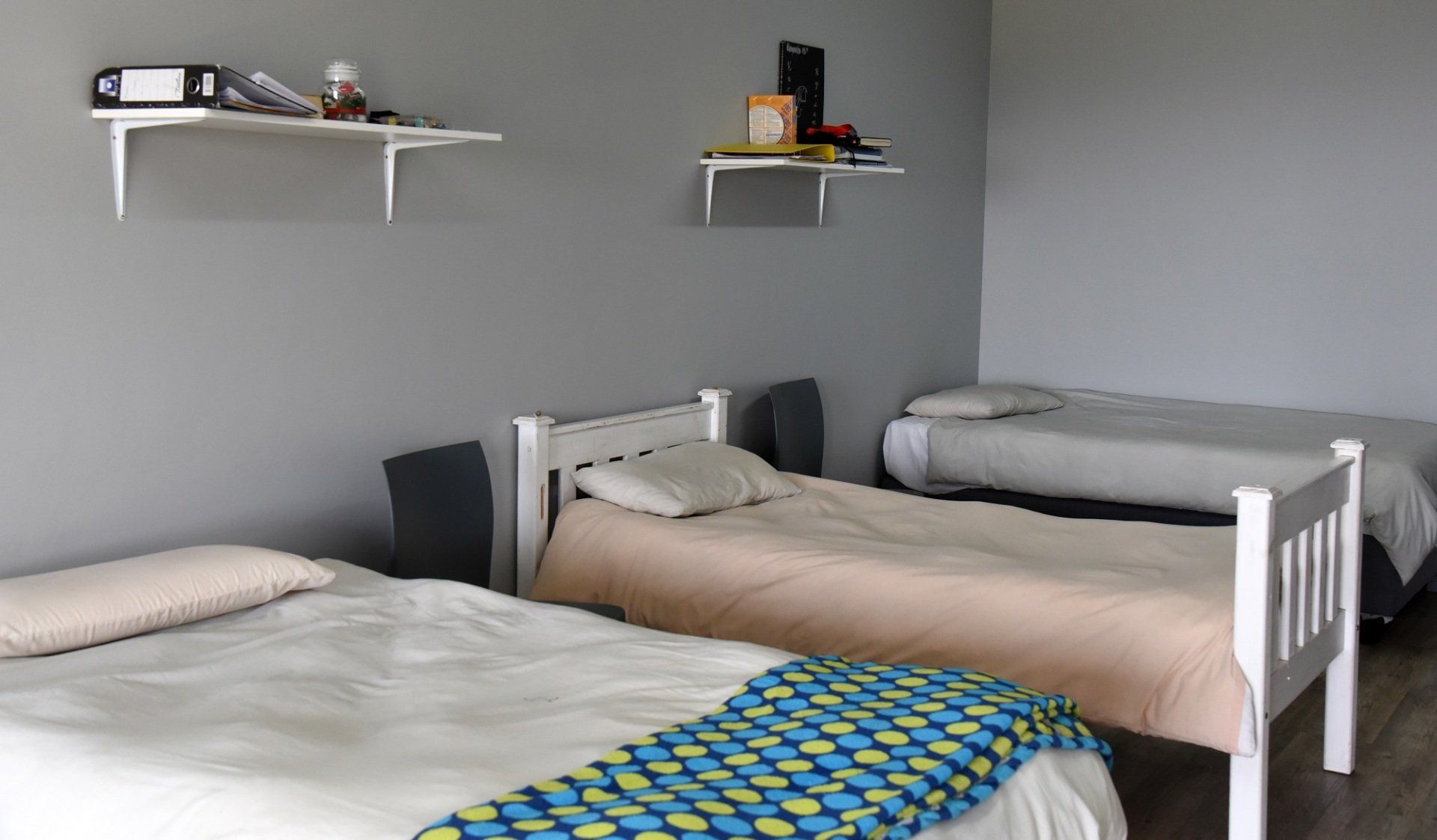 A bedroom with three beds and two shelves on the wall.