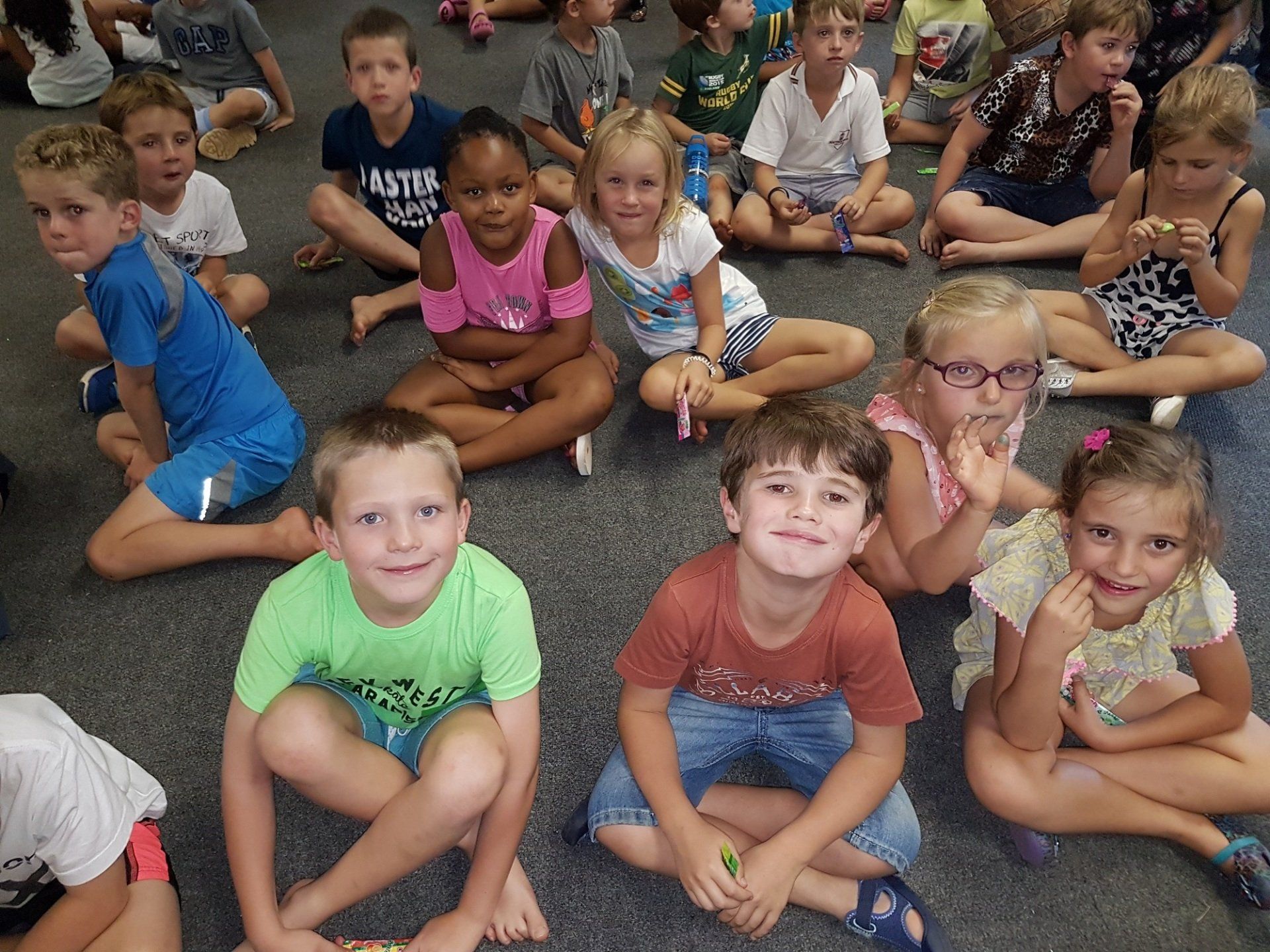 A group of children are sitting on the floor with one boy wearing a shirt that says ' abercrombie & fitch ' on it