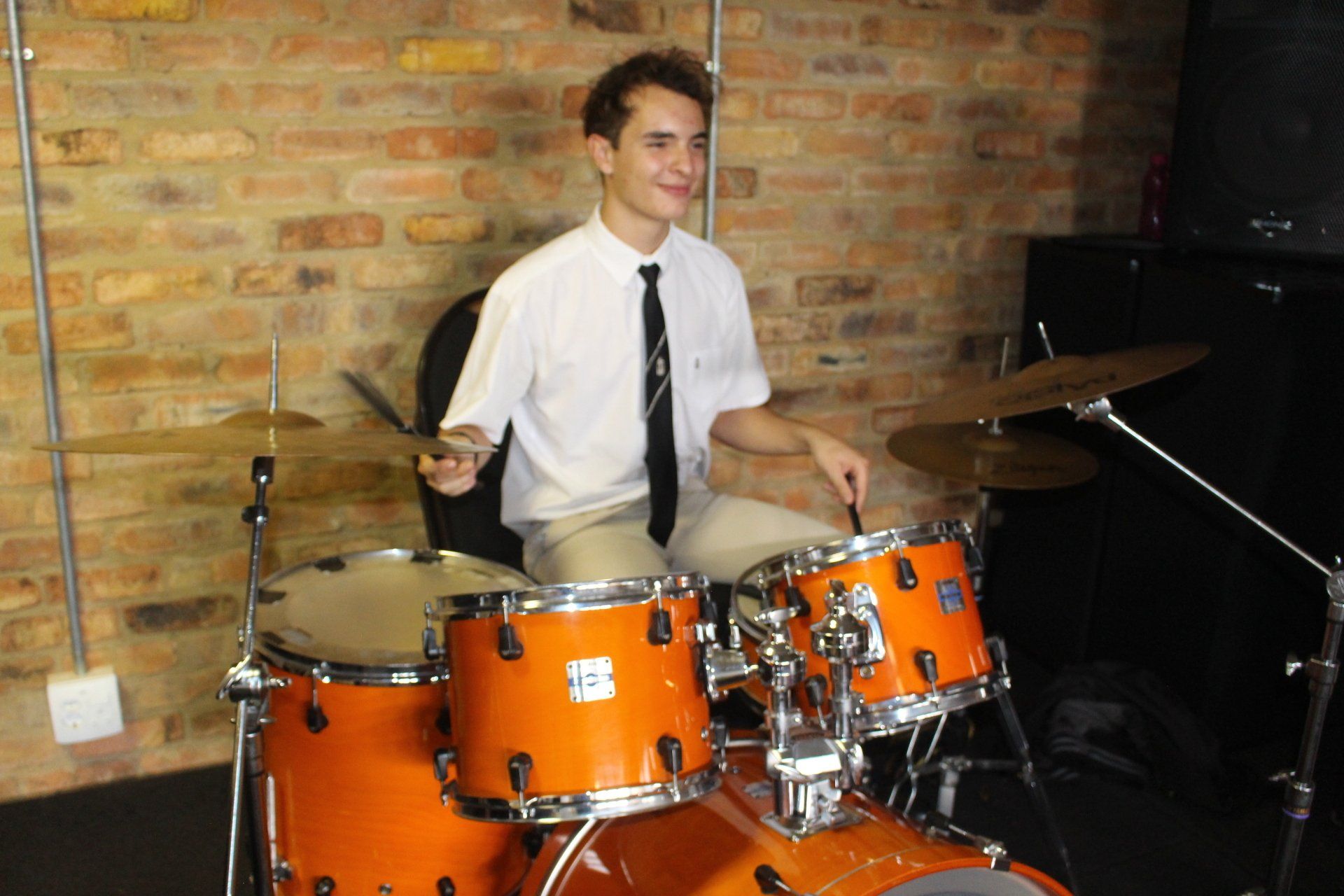 A young man is playing drums in front of a brick wall