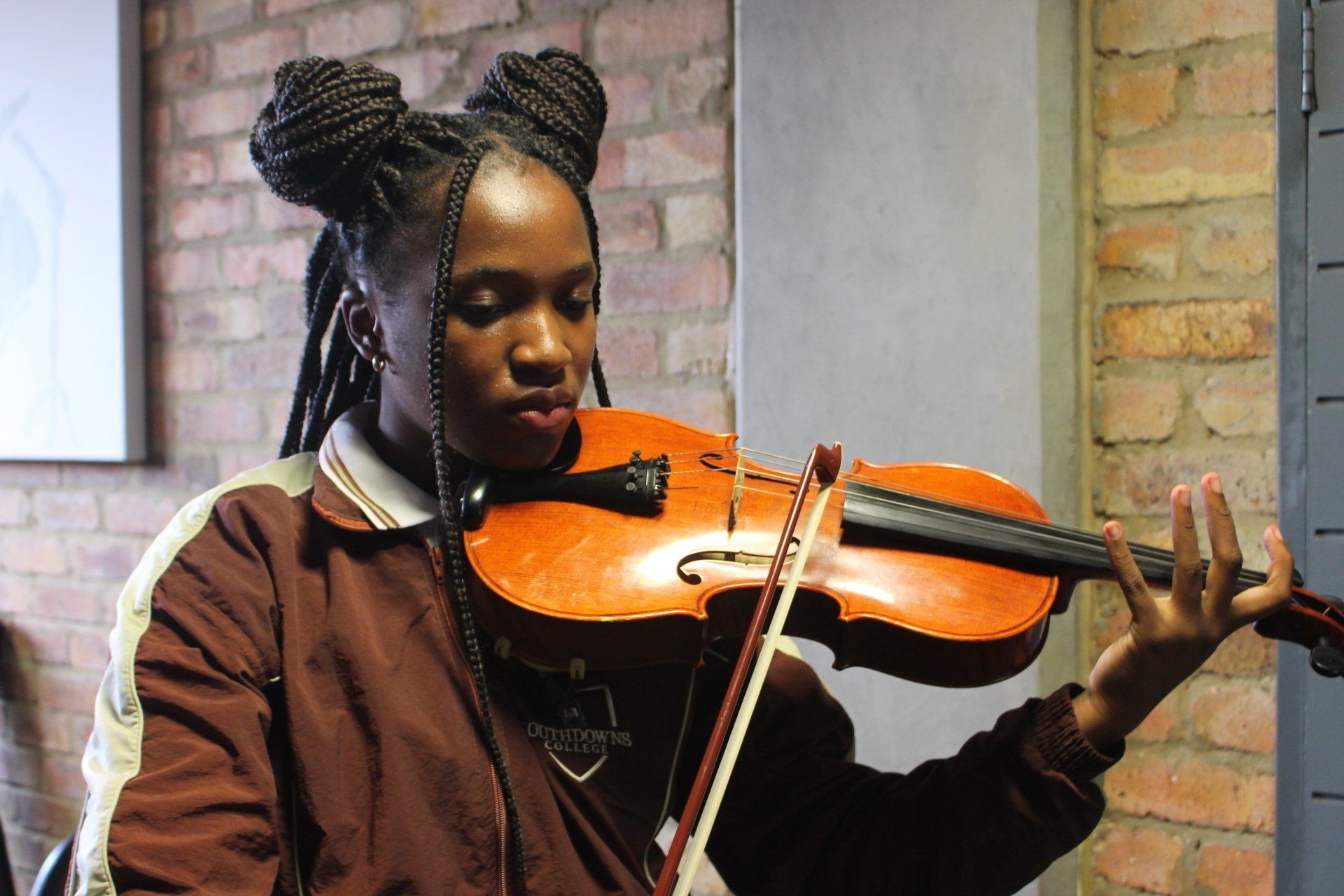 A young woman is playing a violin in front of a brick wall.
