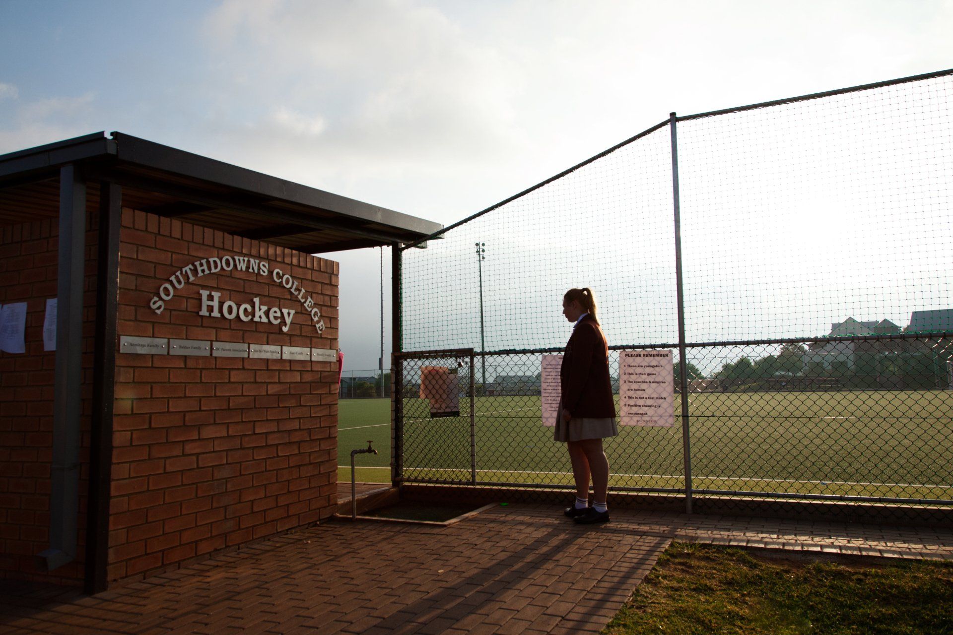 A girl is standing in front of a brick building that says hockey.