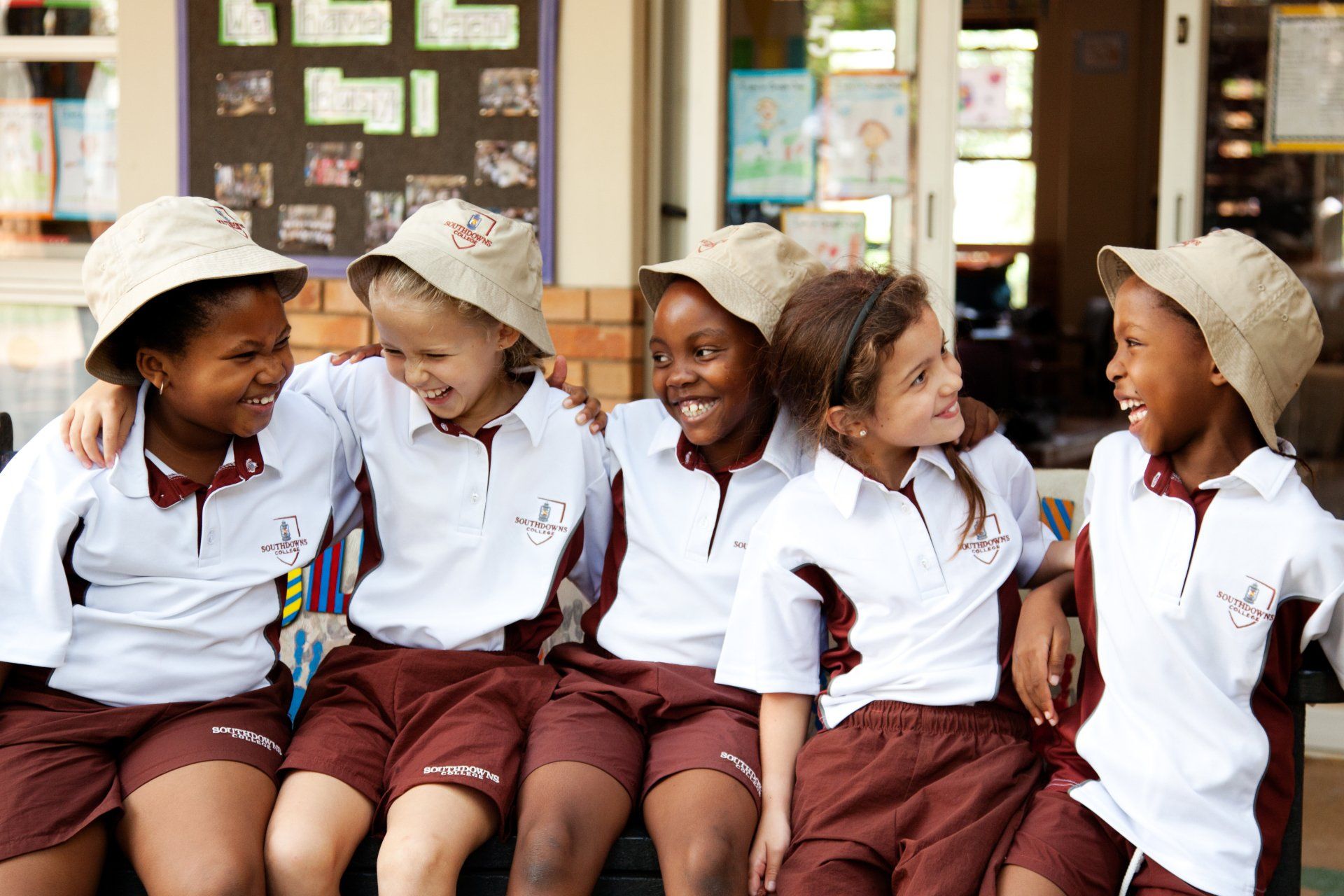 A group of children are sitting on a bench with their arms around each other.