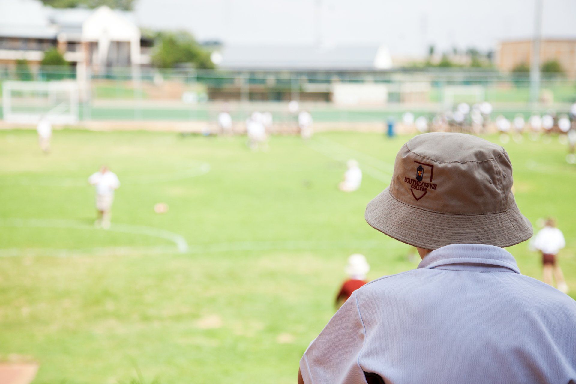 A man wearing a hat is watching a soccer game on a field.