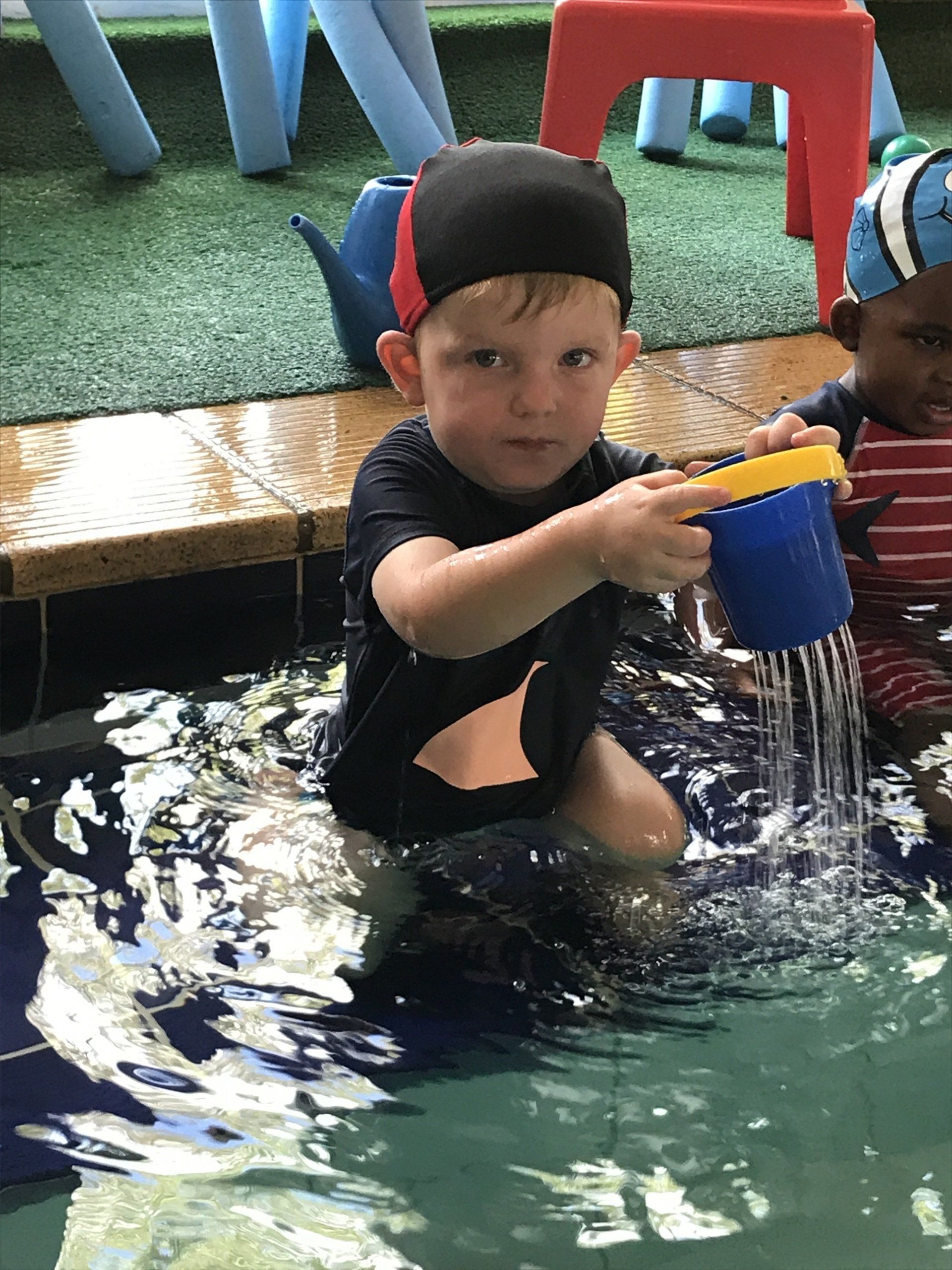 A young boy is playing in a swimming pool with a blue cup.