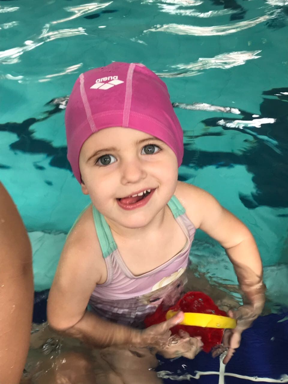A little girl wearing a pink swim cap is swimming in a pool