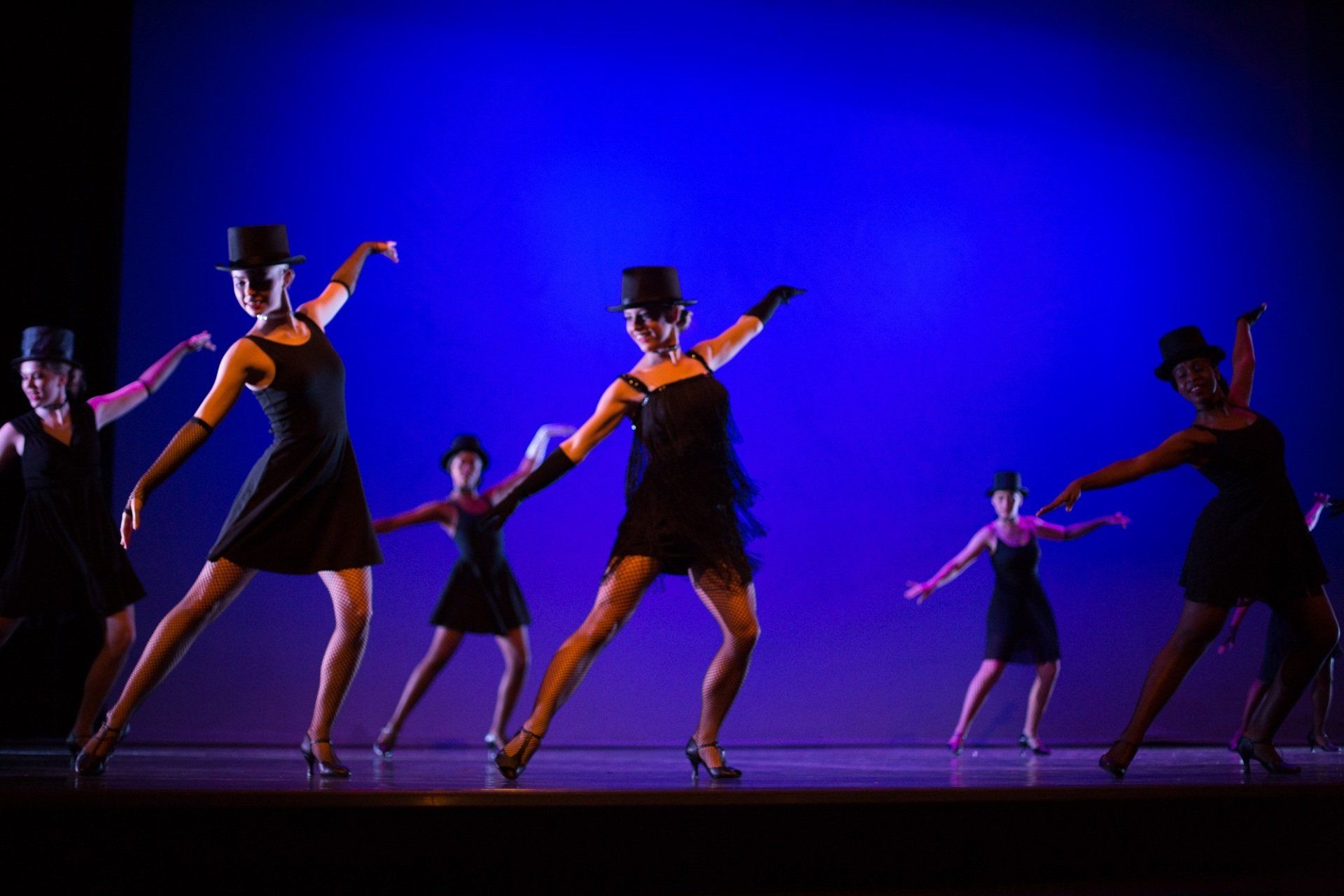 A group of women are dancing on a stage in front of a blue background.