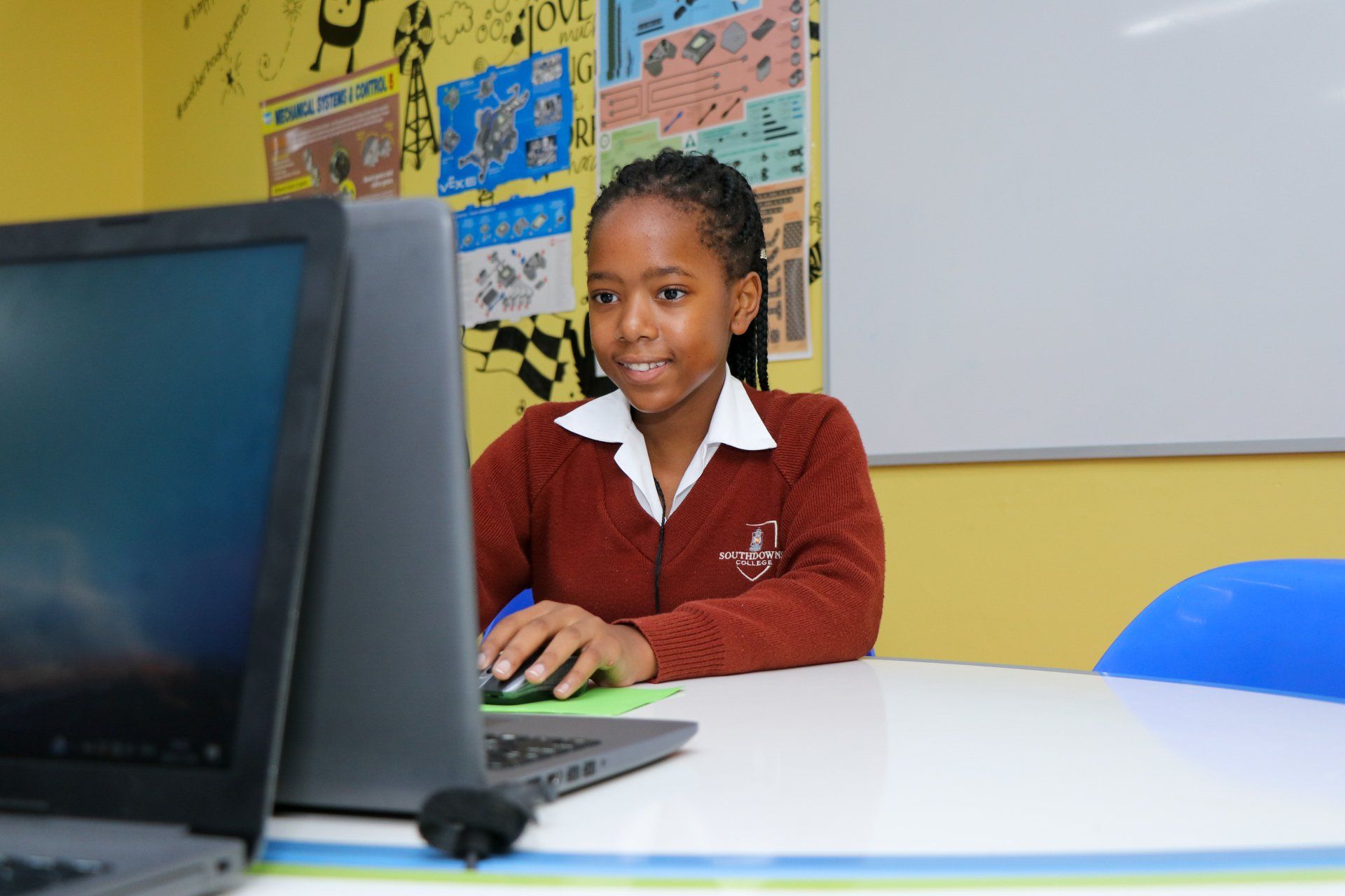 A young girl is sitting at a desk in front of a laptop computer.