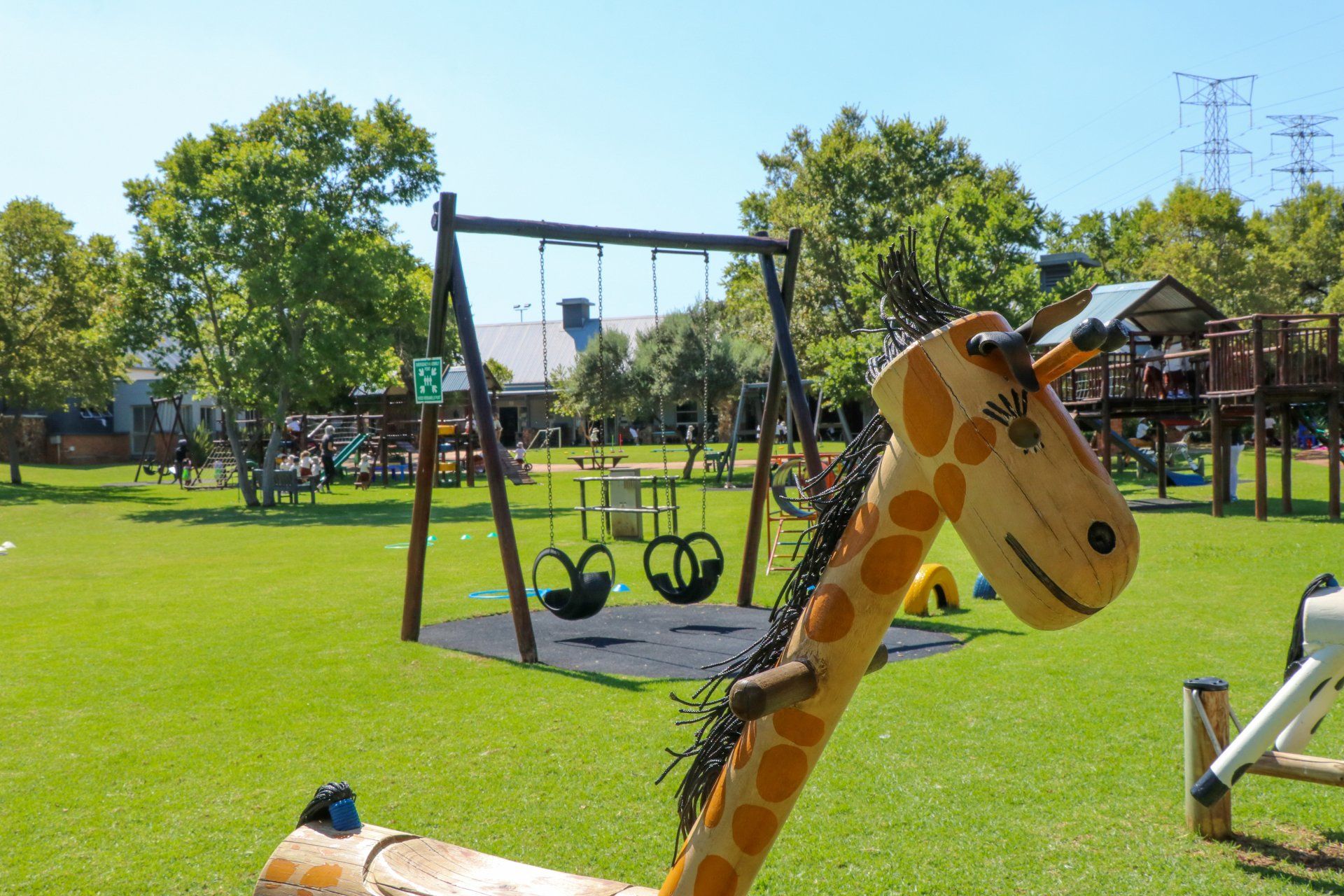 A giraffe shaped rocking horse is sitting in the grass in a park.