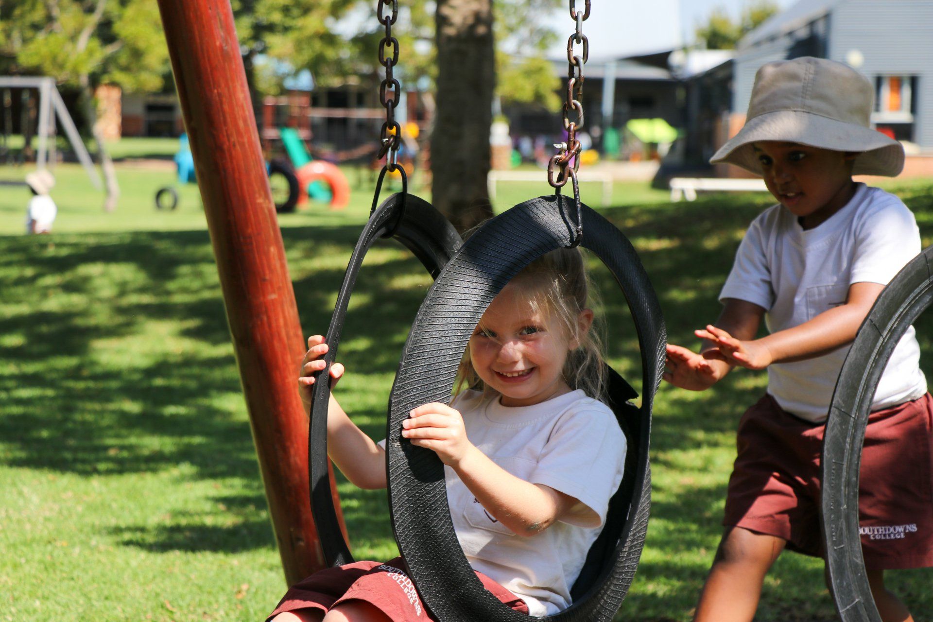 Two children are playing on a tire swing in a park.