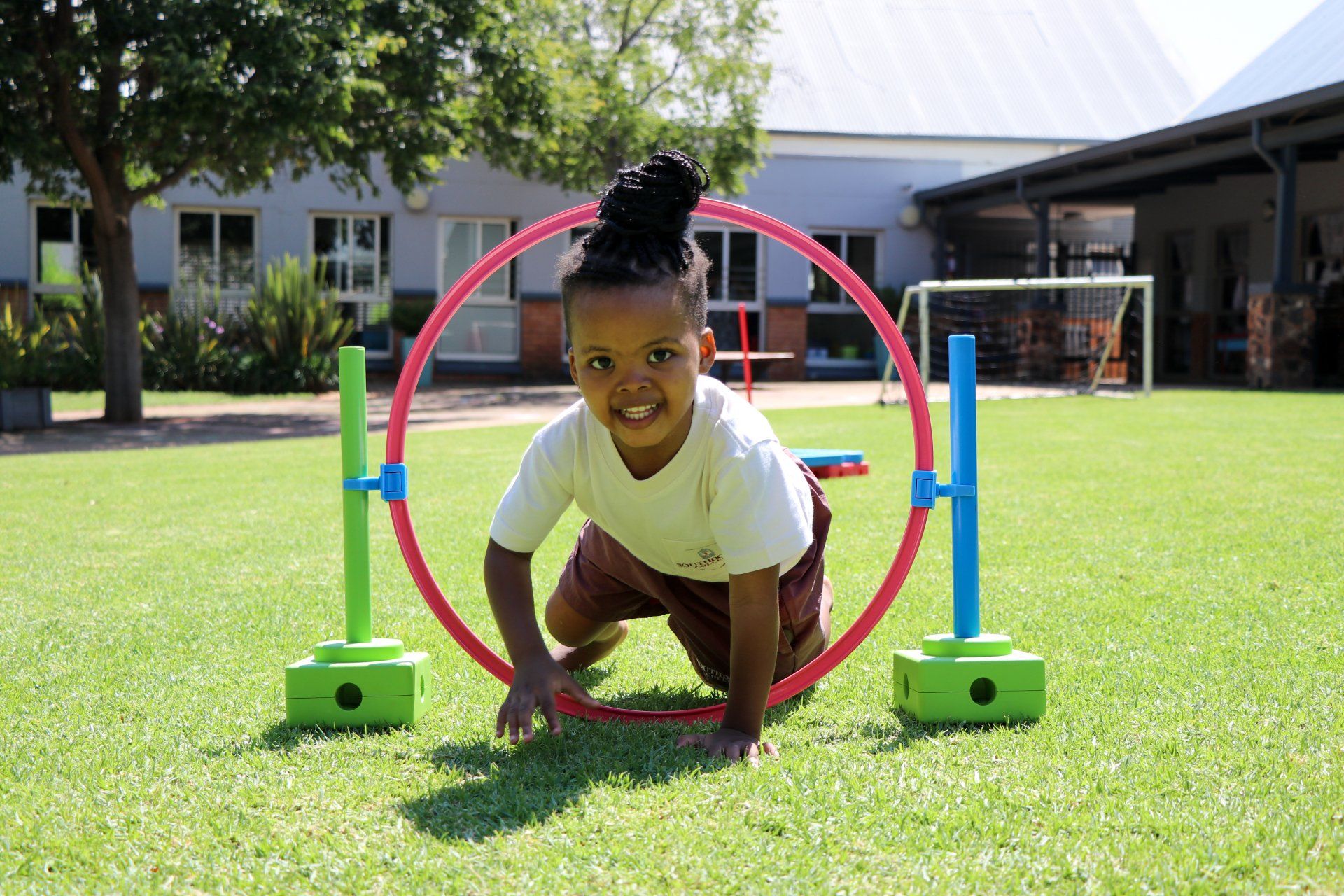 A little girl is crawling through a hula hoop on the grass.