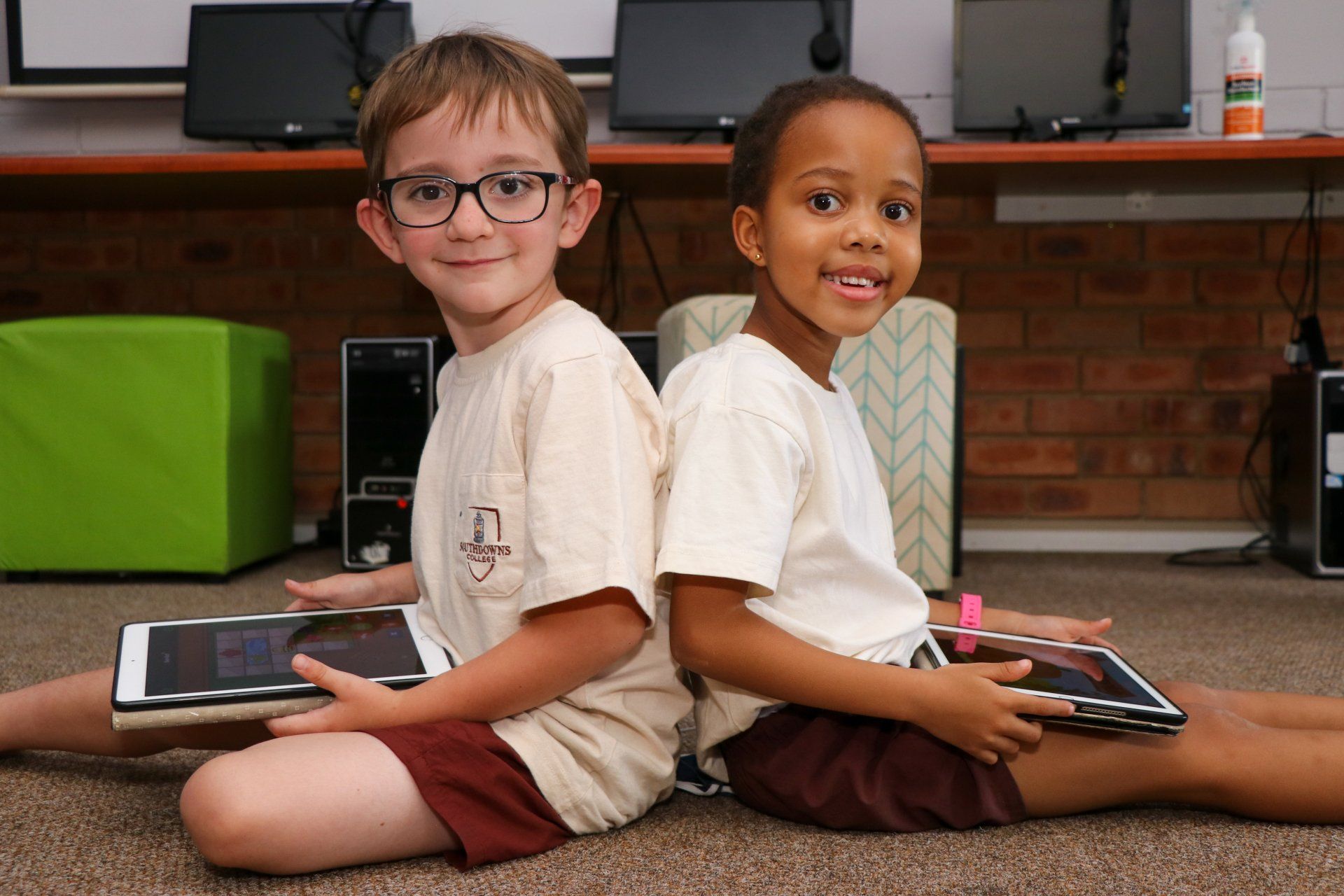 a boy and a girl are sitting back to back on the floor holding tablets .