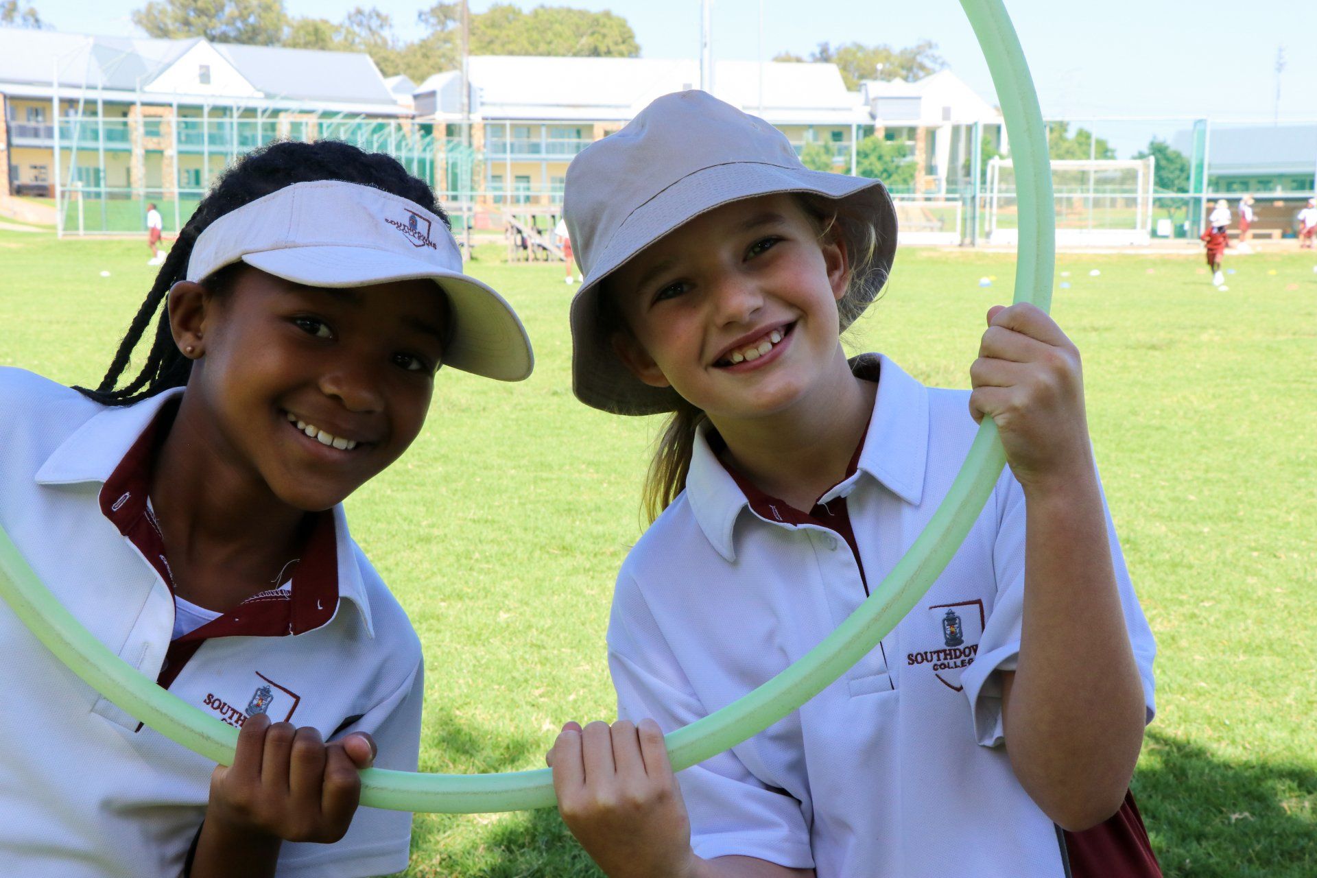 Two girls are holding hula hoops in a field and smiling