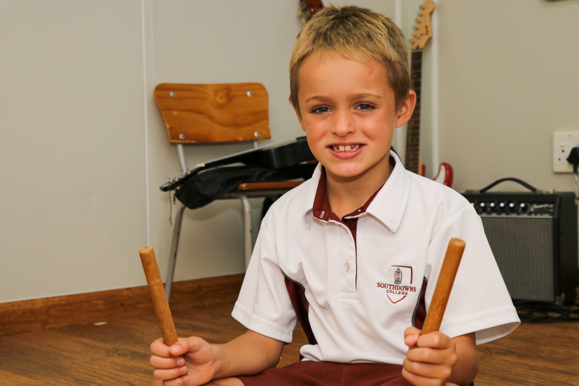 A young boy is sitting on the floor holding a pair of drumsticks