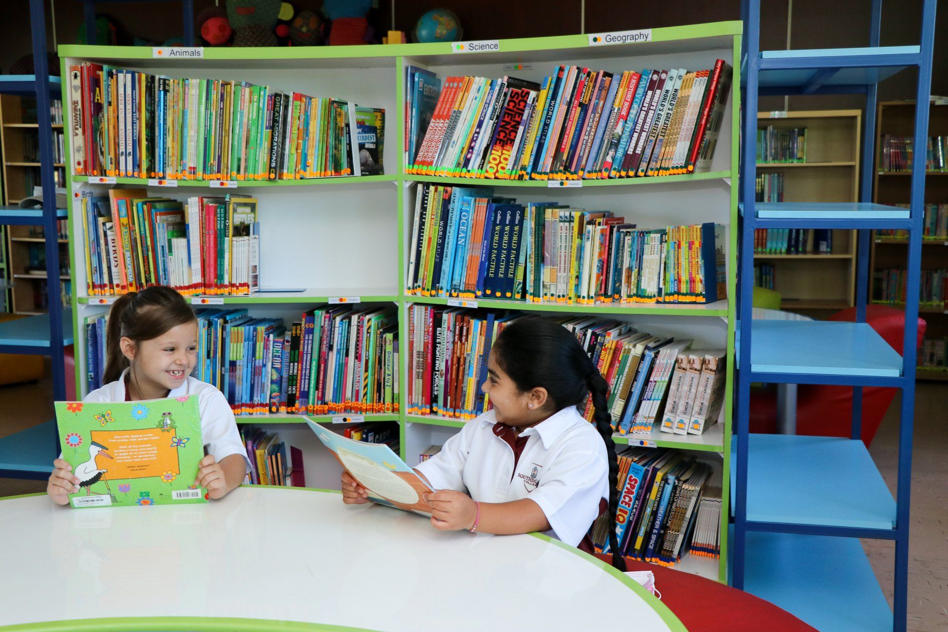 Two young girls are reading books in a library.