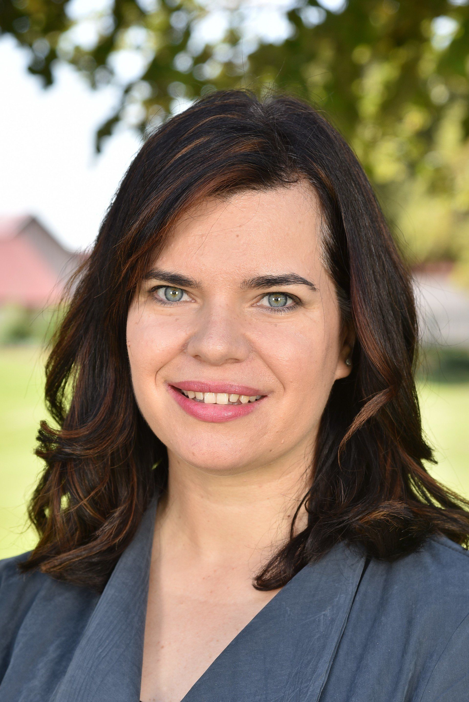 A woman with long dark hair and blue eyes is smiling for the camera.