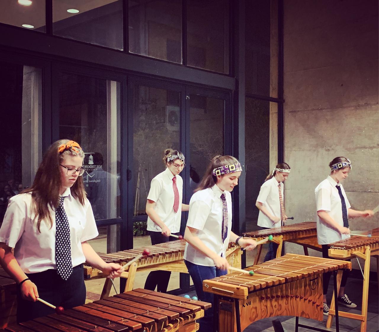 A group of people are playing xylophones in front of a building