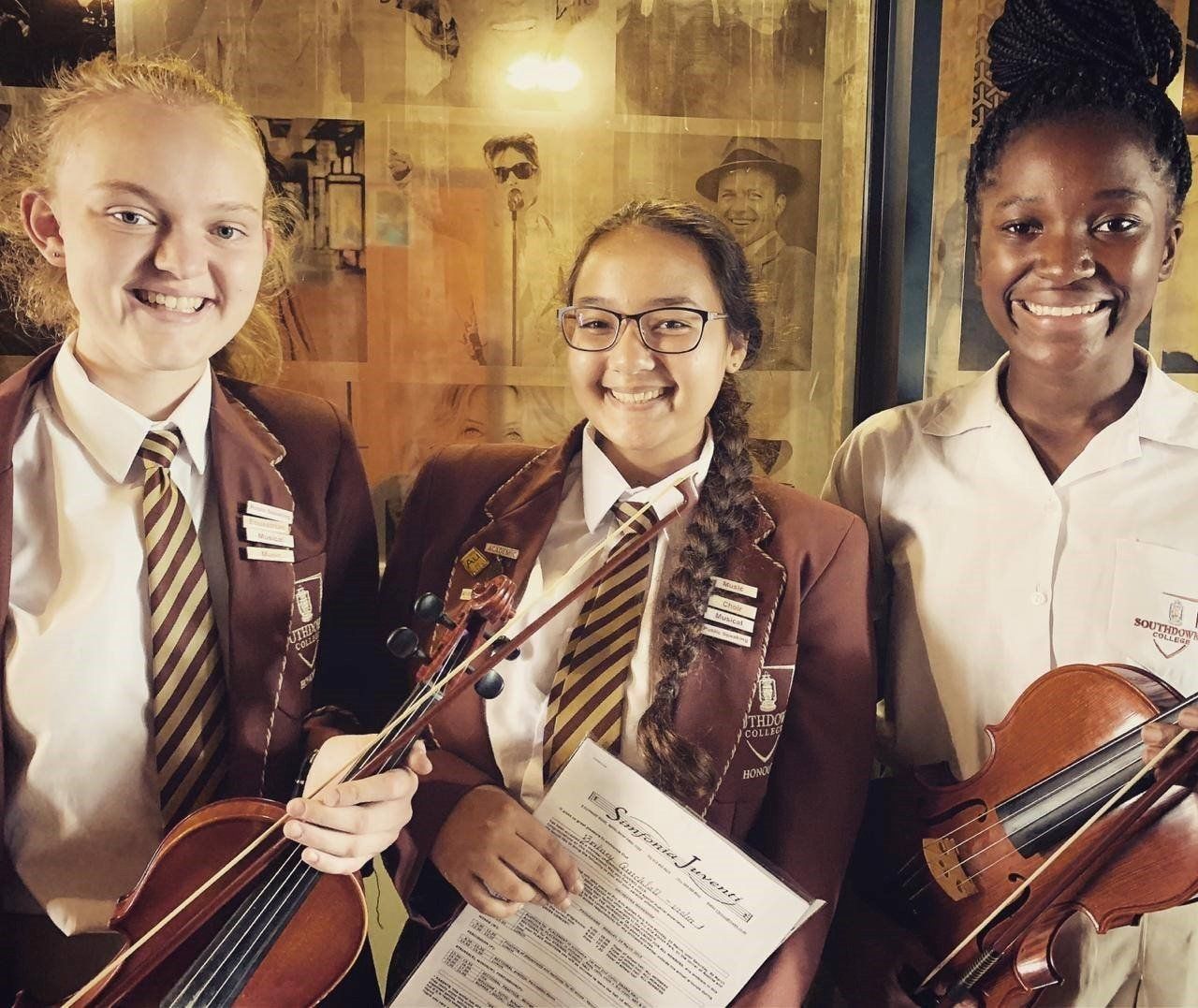 Three girls are holding violins and smiling for the camera