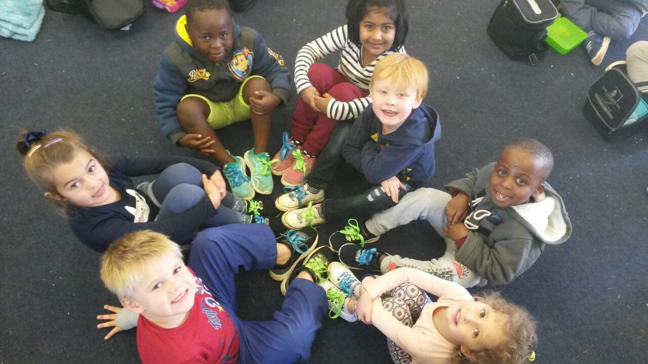 A group of children are sitting in a circle with their shoes on the floor