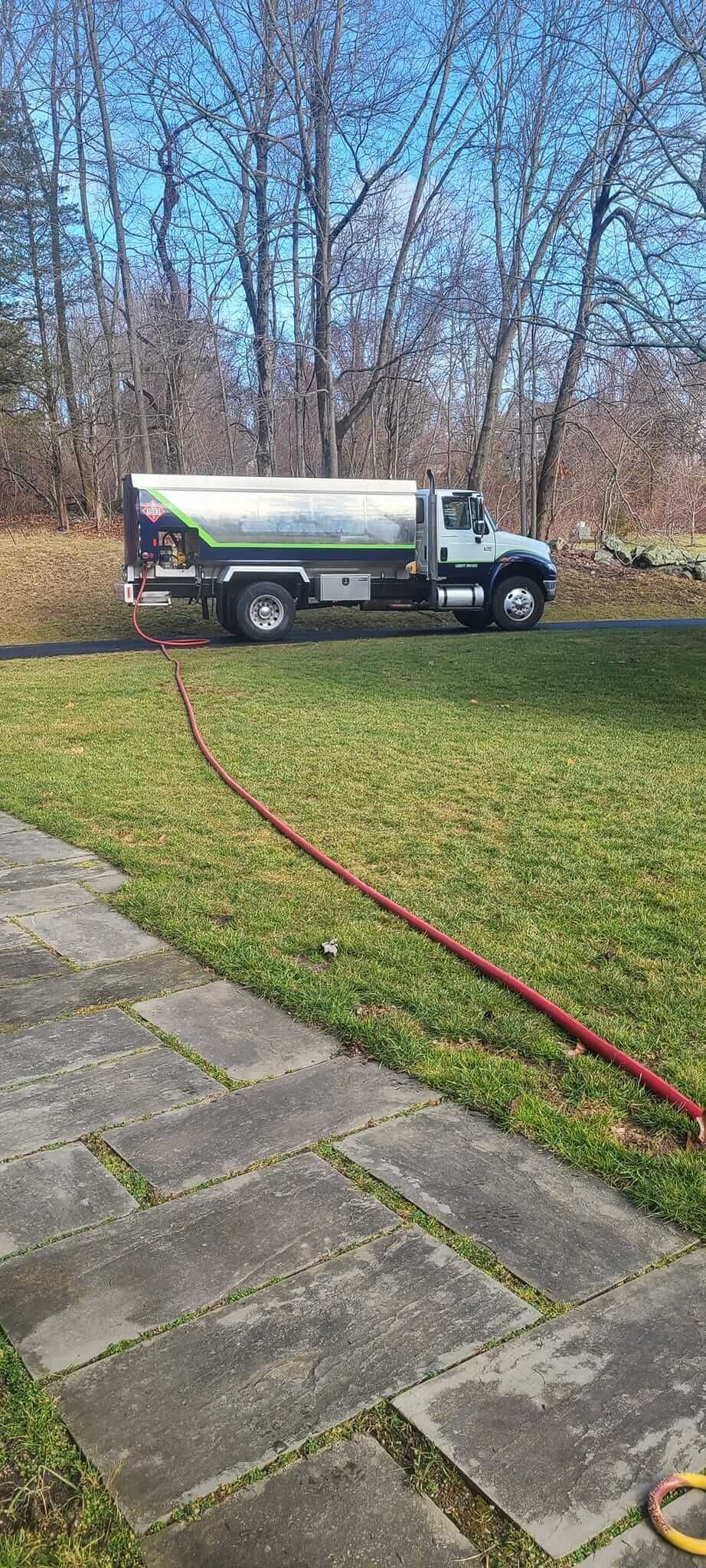 A tanker truck is parked in a grassy yard next to a sidewalk.