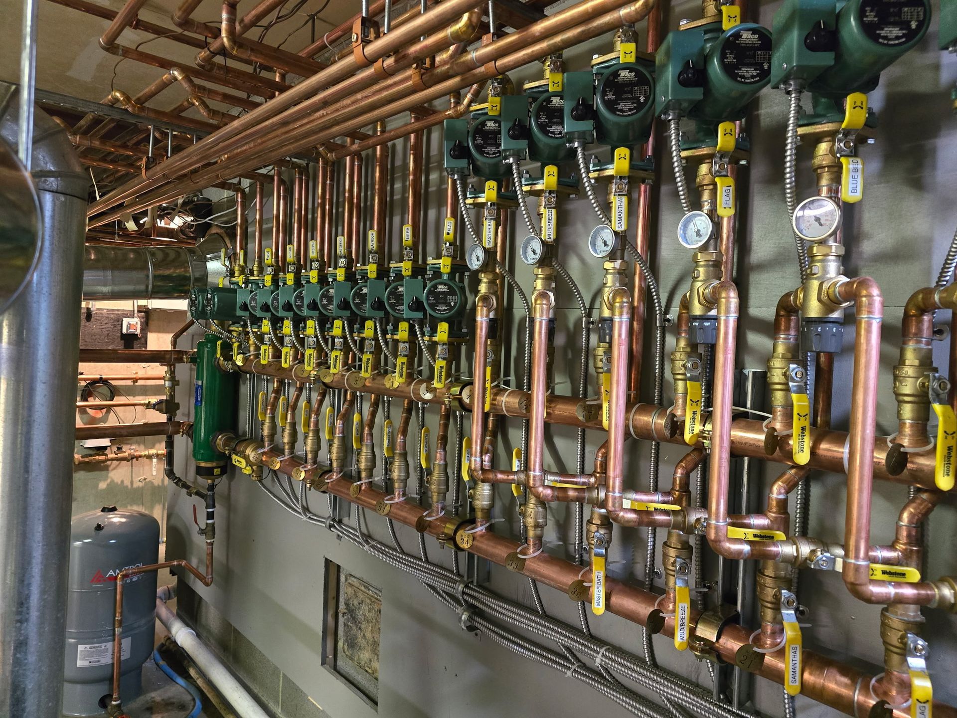 A row of copper pipes with yellow valves are lined up on a wall.