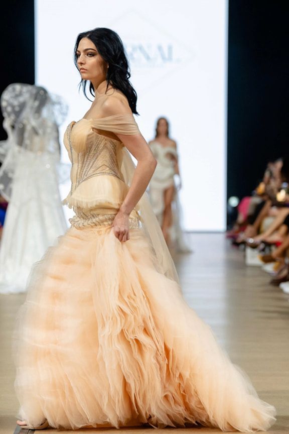 A Woman in a Long Dress is Walking Down a Runway at a Fashion Show — Eternal Weddings & Couture In Woolner, NT