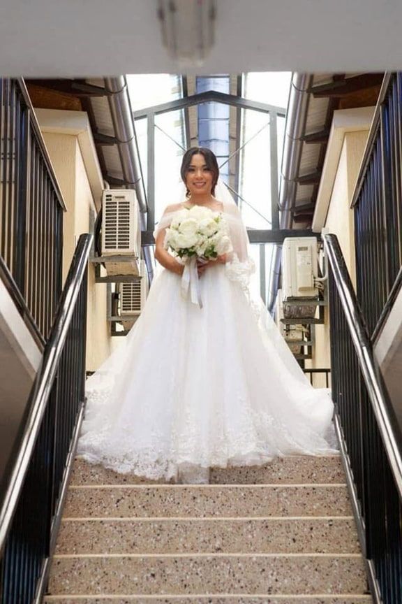 A Bride in a Wedding Dress on a Set of Stairs Holding a Bouquet of Flowers — Eternal Weddings & Couture In Woolner, NT