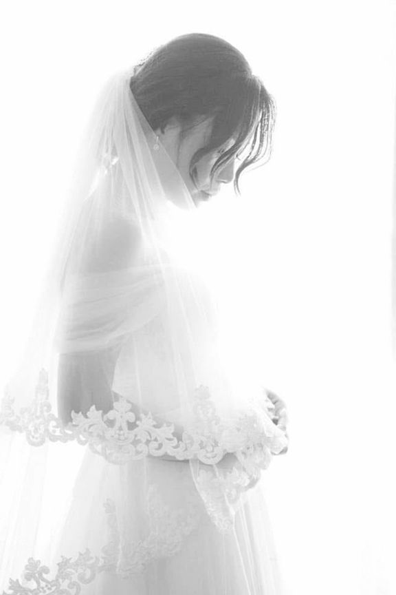 A Pregnant Woman in a Wedding Dress and Veil is Standing in Front of a Window — Eternal Weddings & Couture In Woolner, NT