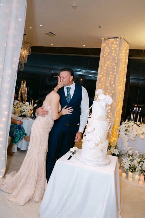 A Bride and Groom Are Kissing in Front of a Wedding Cake — Eternal Weddings & Couture In Woolner, NT